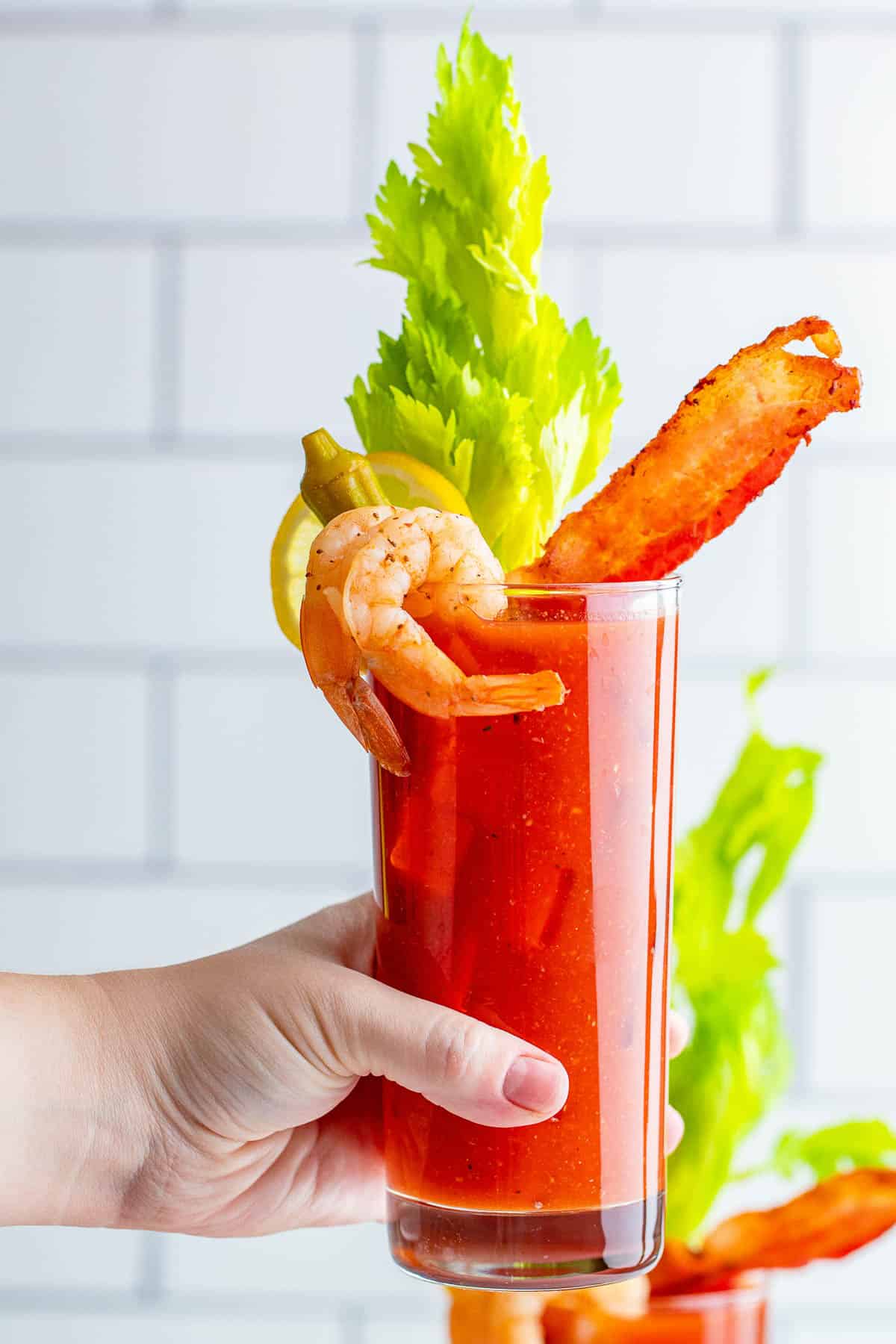 Bloody mary con camarones, bacon y apio en la mano de una mujer.