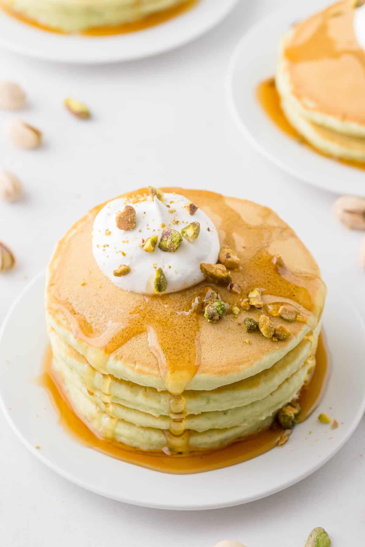 Panqueques cubiertos con jarabe, crema batida y pistachos.