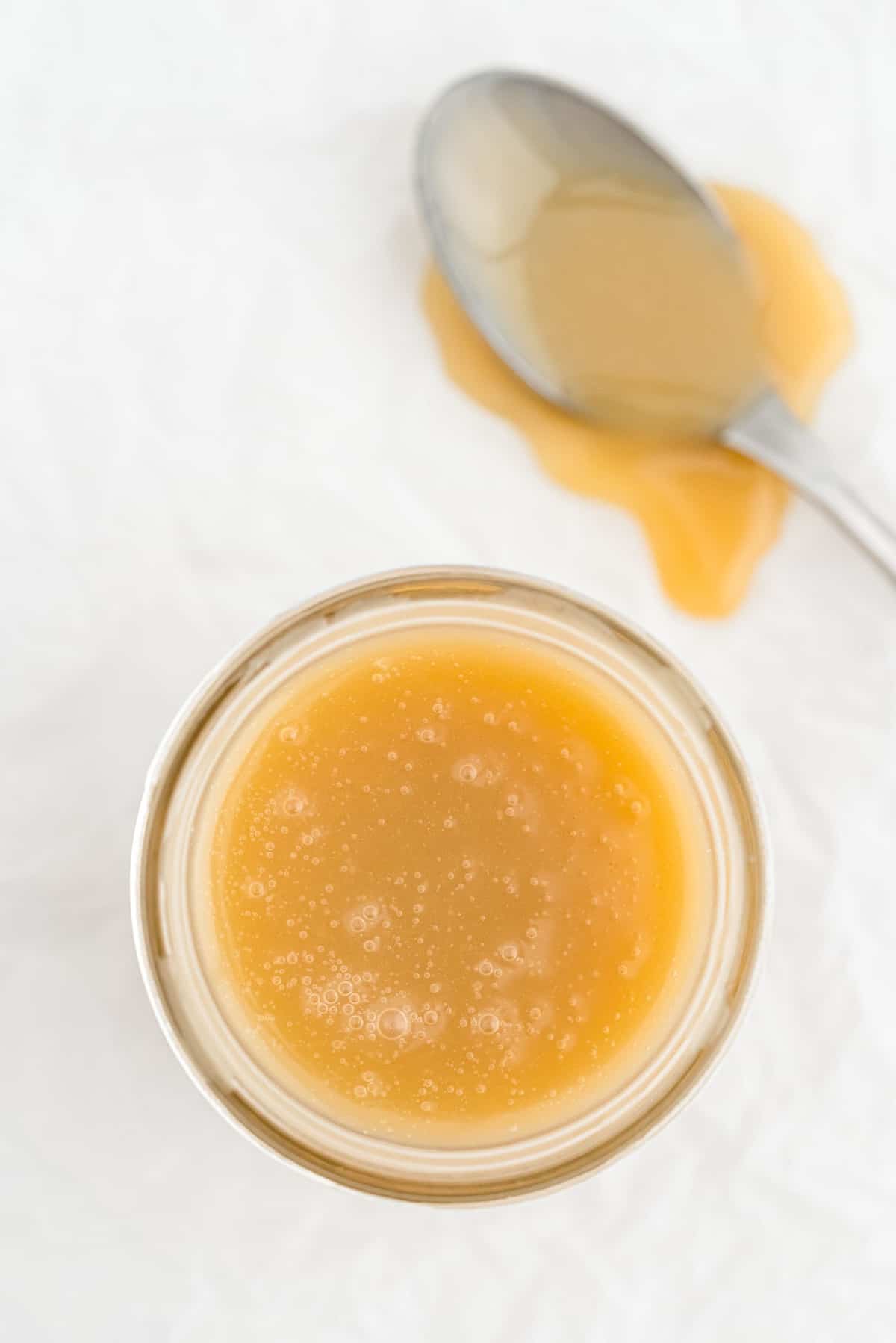 Tarro de salsa de caramelo sobre una superficie gris claro, con una cuchara al lado cubierta de caramelo.