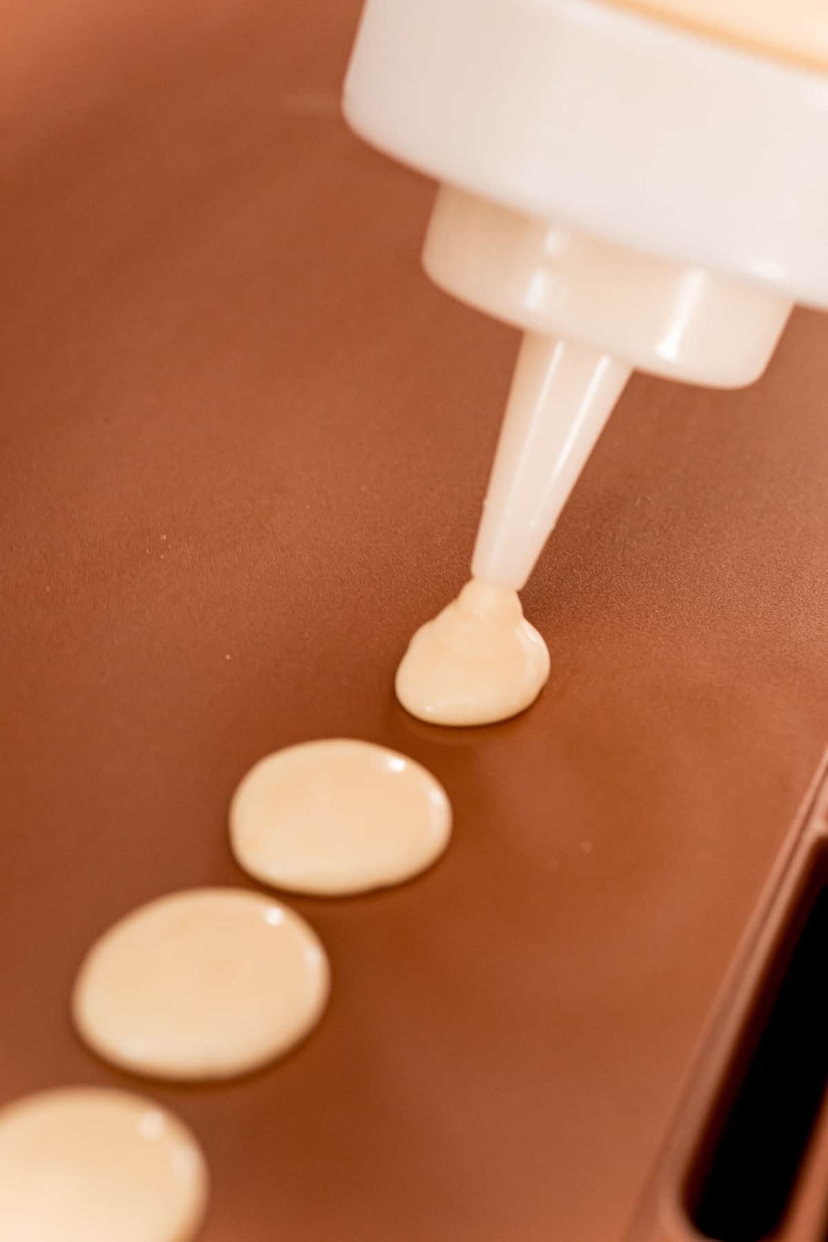 Masa de panqueques siendo puesta en la plancha en pequeñas cantidades usando una botella exprimible.