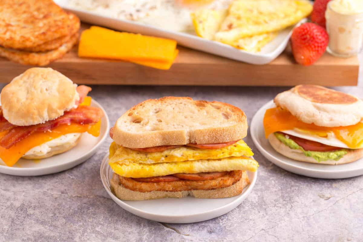 Tres diferentes sándwiches de huevo en pequeños platos blancos.