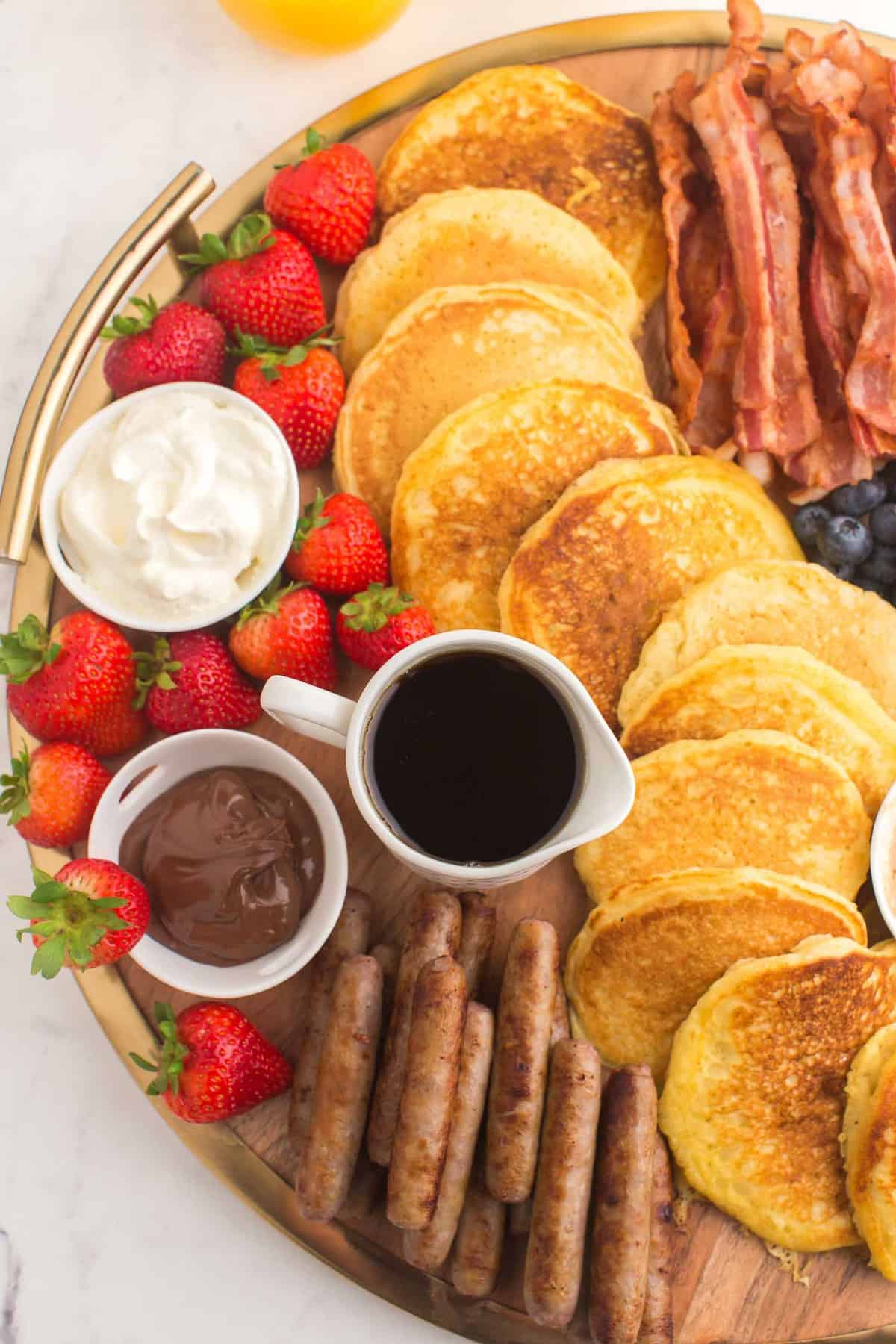 Panqueques, tocino, jarabe, salchichas y fresas en una tabla.