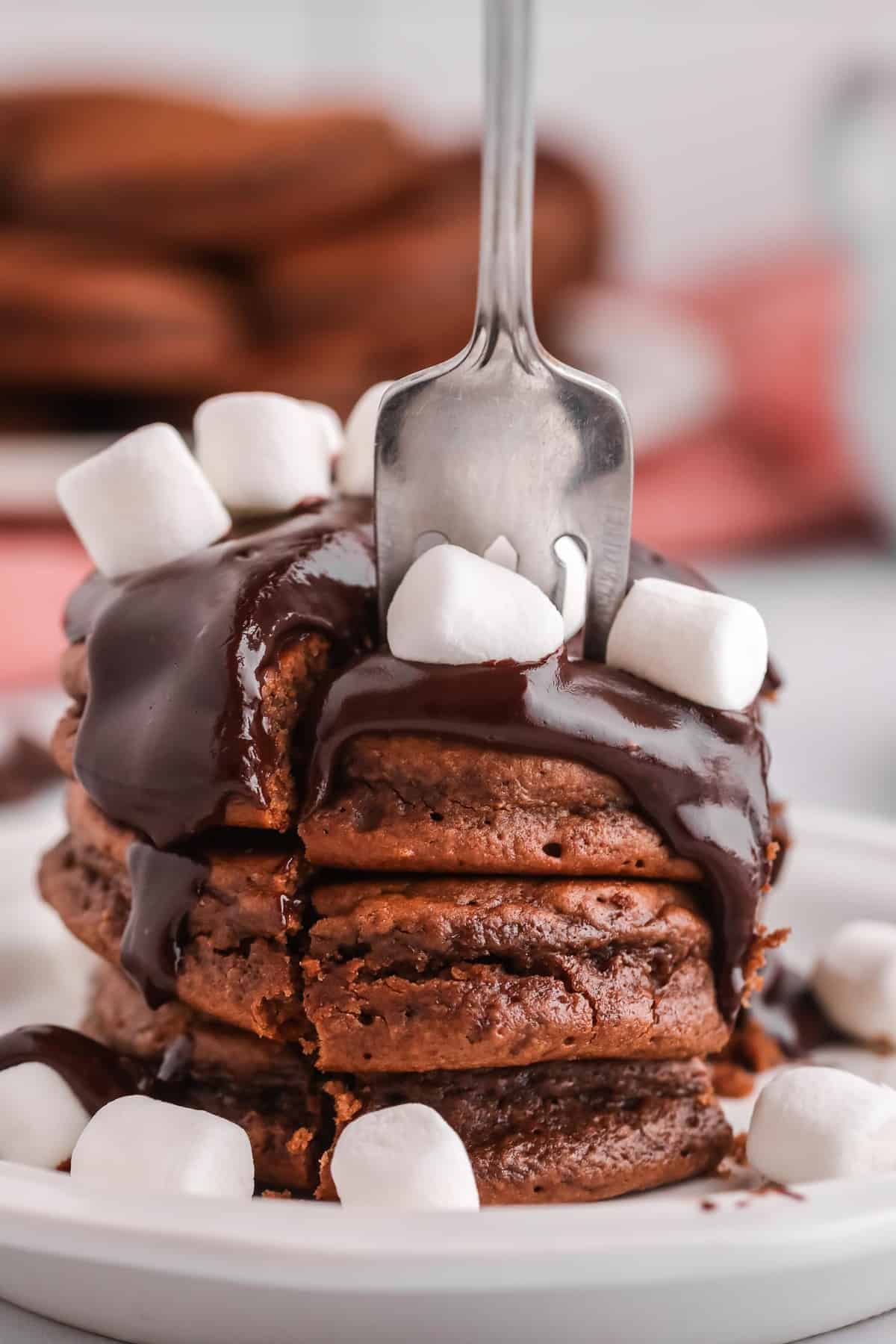 Un tenedor cavando en un montón de panqueques de chocolate con salsa de chocolate.