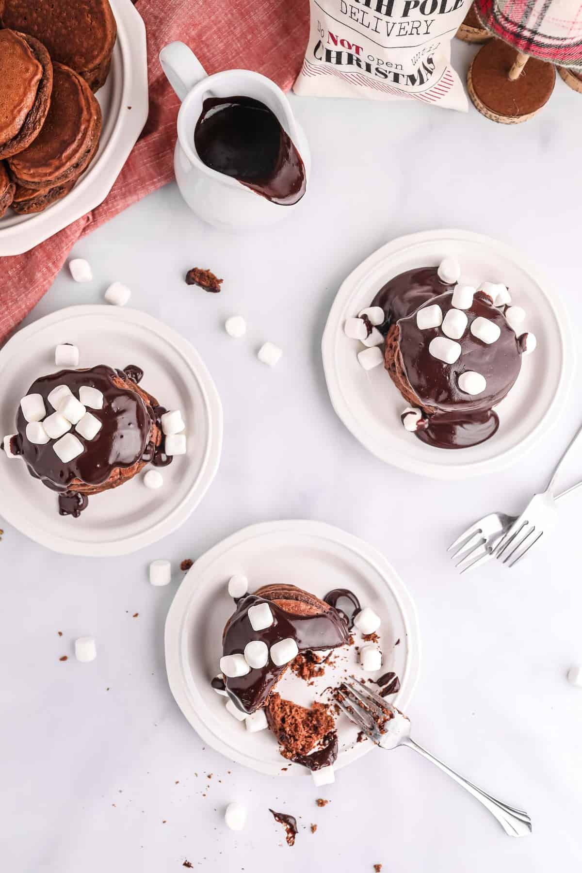 Tres platos de panqueques con salsa de chocolate y mini malvaviscos en la parte superior.