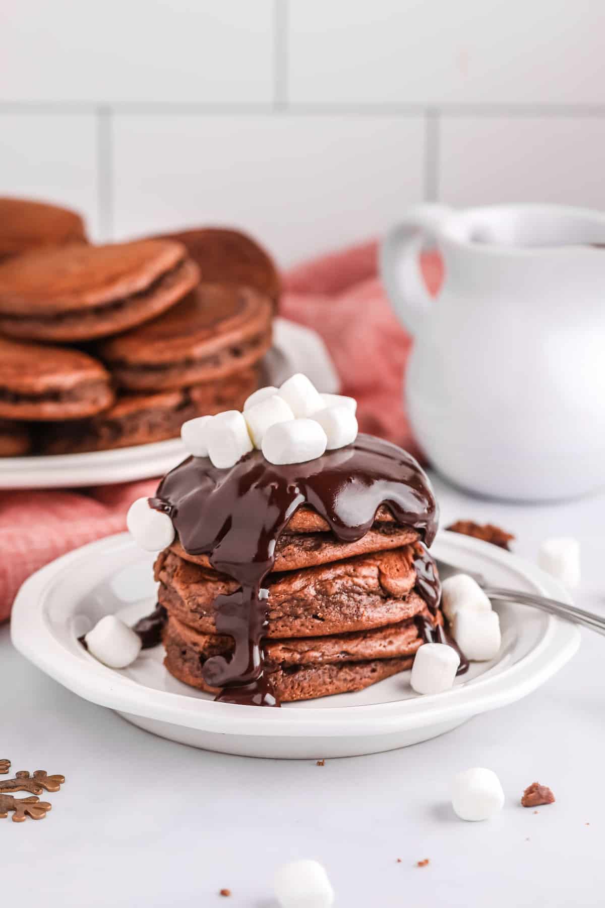 Una pila de panqueques de chocolate caliente cubiertos con jarabe de chocolate y malvaviscos.