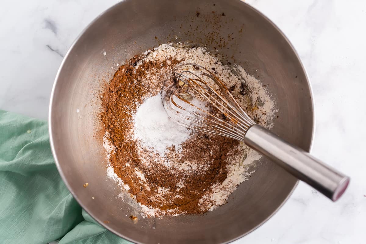 Ingredientes secos y un batidor de plata en un tazón de acero inoxidable.