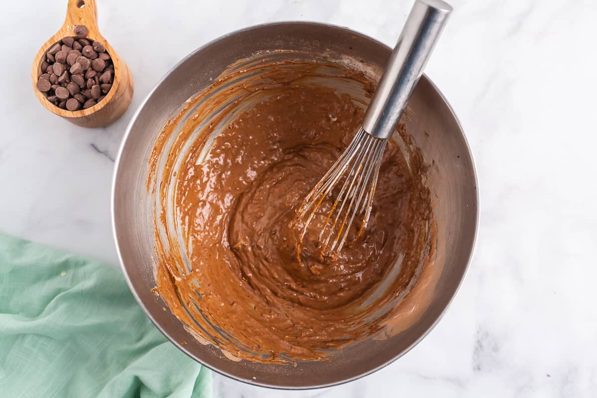 Masa de panqueques de chocolate y batidor de plata en un tazón de acero inoxidable.
