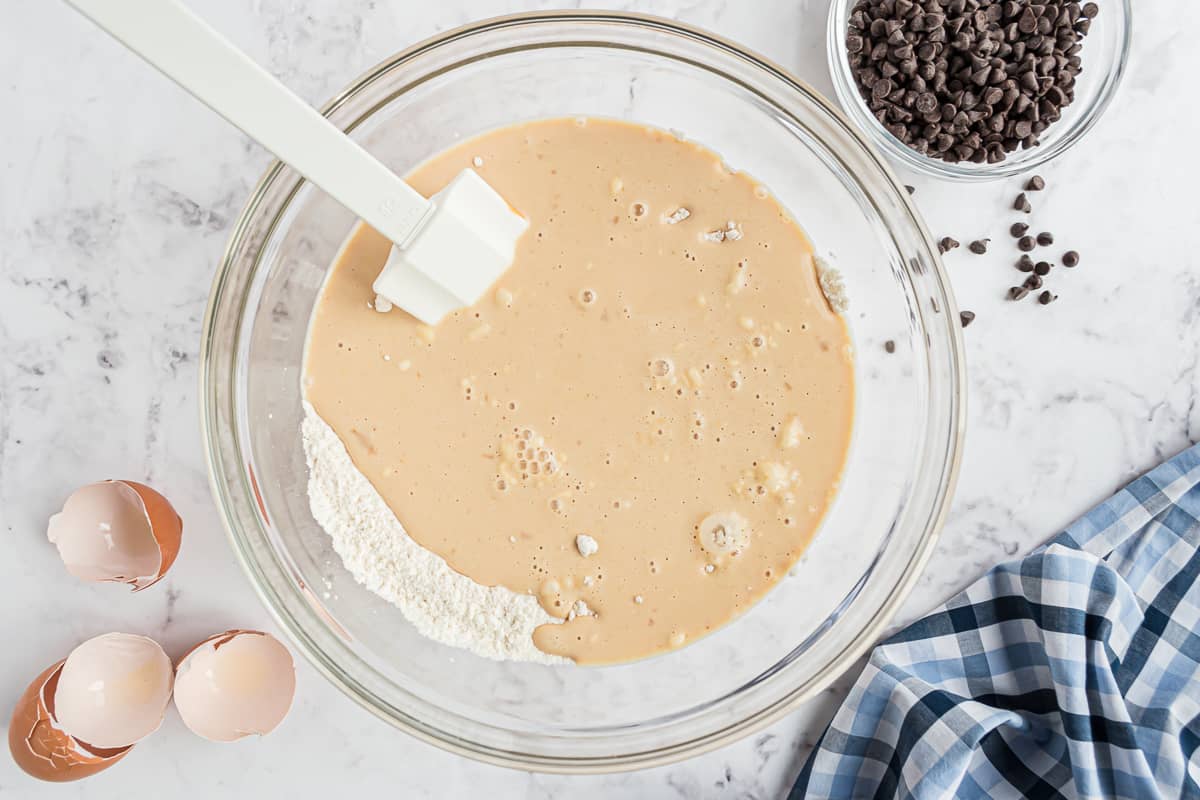 Ingredientes húmedos y secos mezclándose con una espátula blanca.