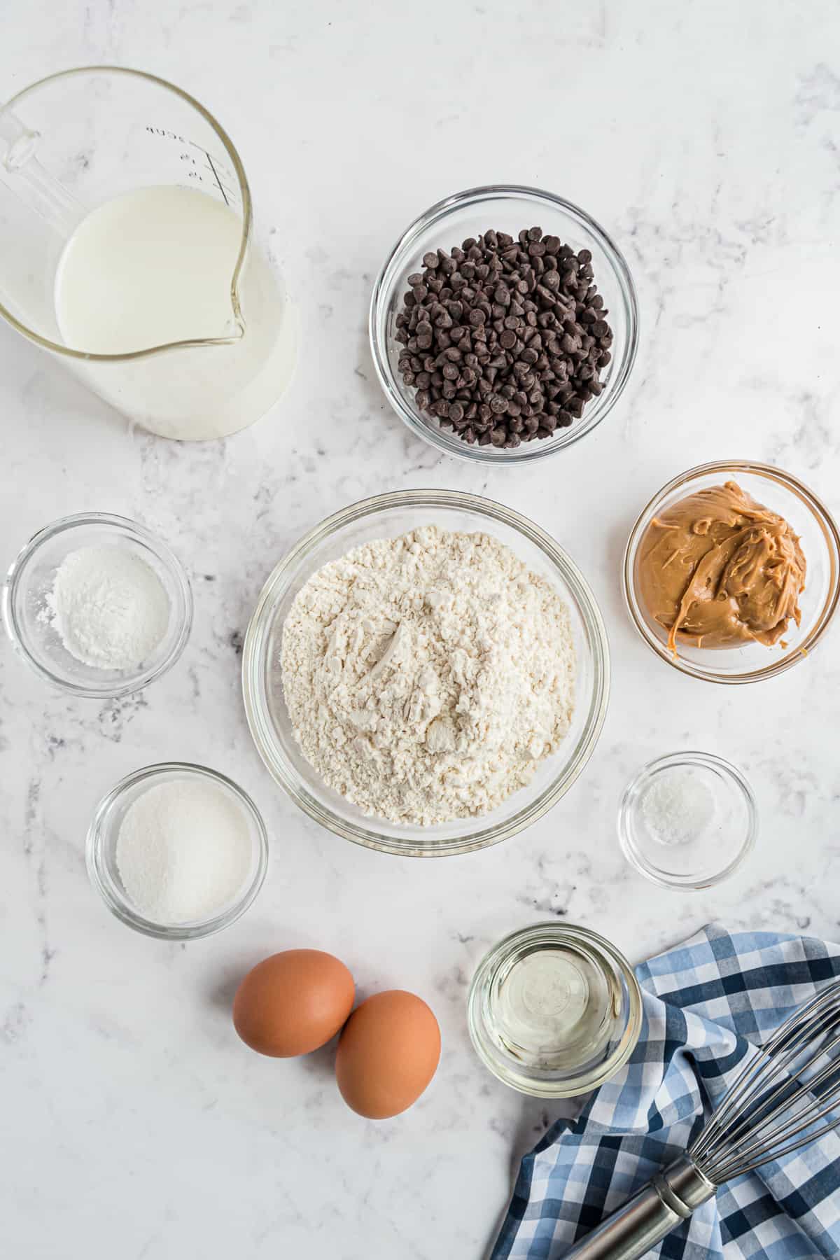 Pequeños tazones de ingredientes, incluyendo mantequilla de cacahuete y chips de chocolate, y huevos marrones.