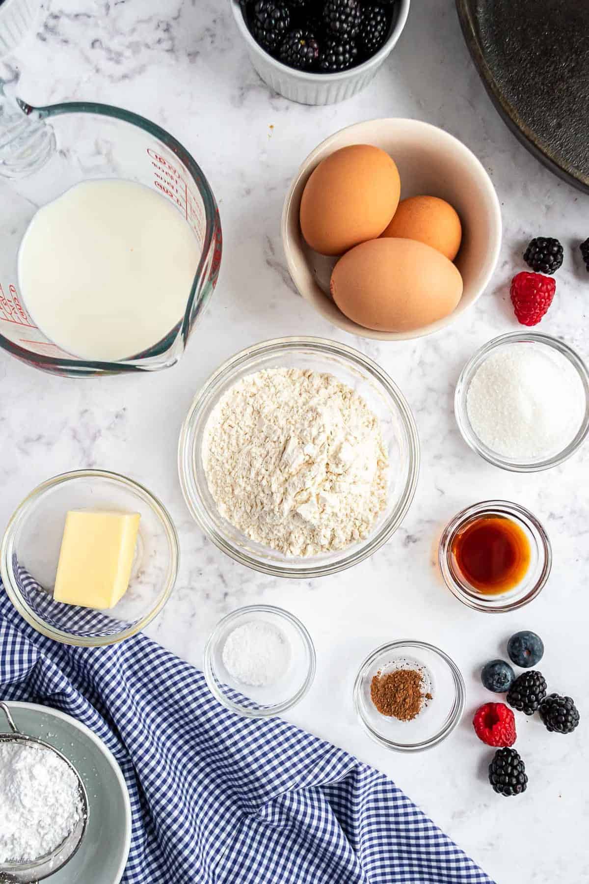 Vista cenital de los ingredientes: harina, leche, huevos, vainilla, mantequilla y más.