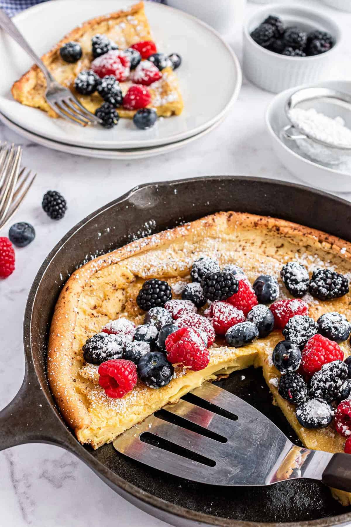 Rebanadas de Dutch baby siendo retiradas de una sartén negra.