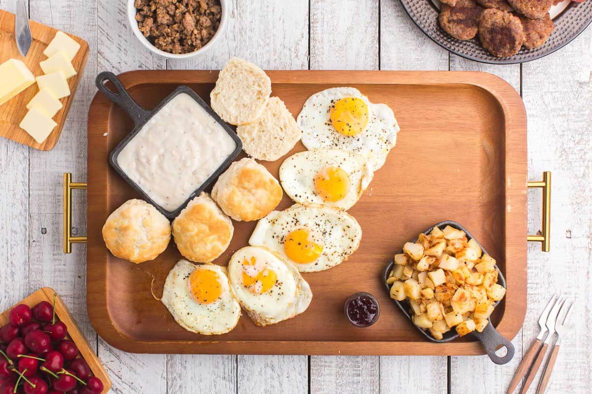 Huevos, panecillos, papas y salsa en una bandeja de madera.
