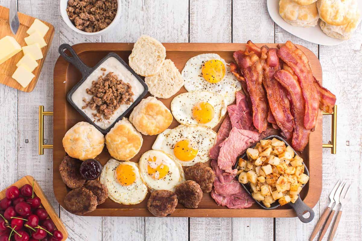 Tabla de desayuno llena de carnes del desayuno, huevos fritos y papas en cubos.