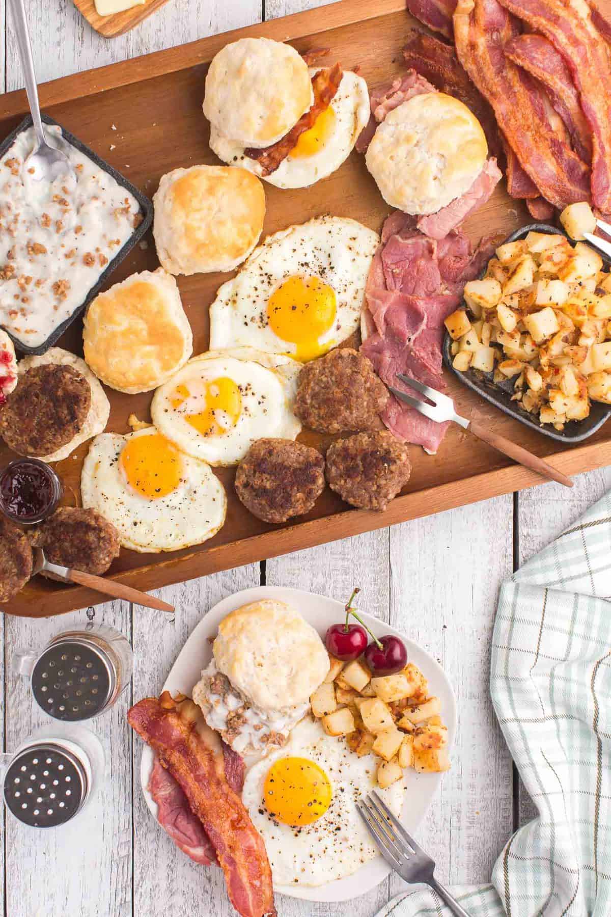 Varios productos del desayuno en una bandeja de madera con un plato lleno cerca.