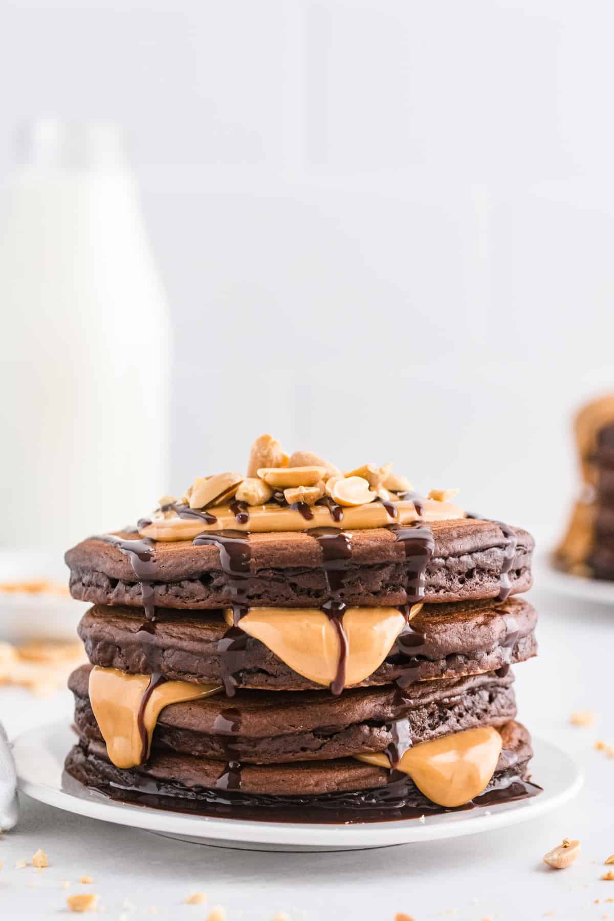 Montón de panqueques goteando con sirope de chocolate y mantequilla de maní derretida.