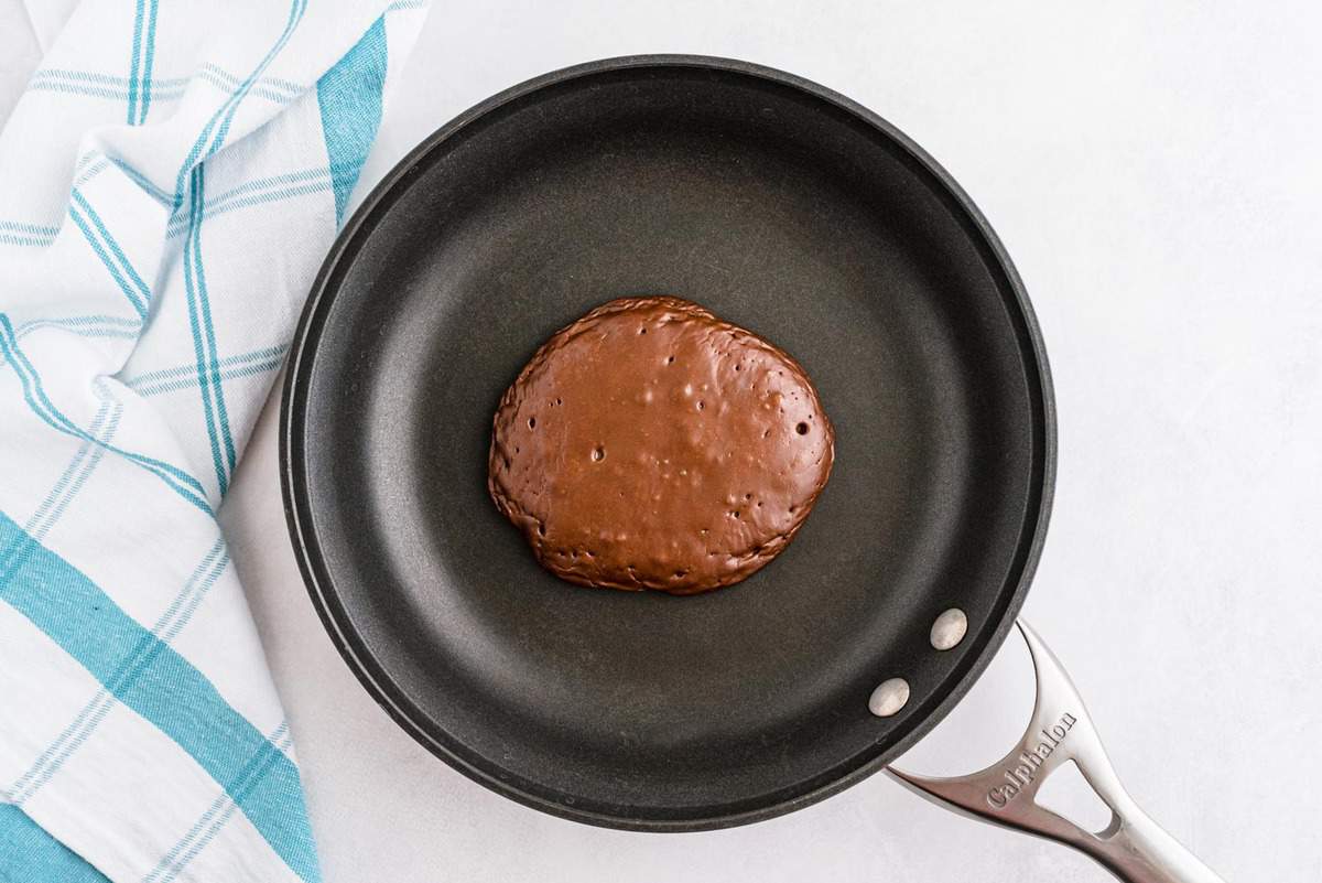 Panqueque de chocolate cocinándose a la mitad en una pequeña sartén negra.