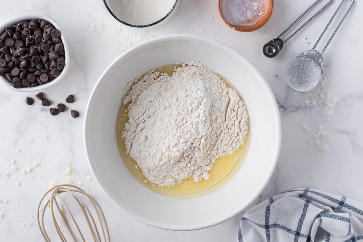 Ingredientes secos para panqueques siendo añadidos a los ingredientes húmedos en un tazón de mezcla blanco.