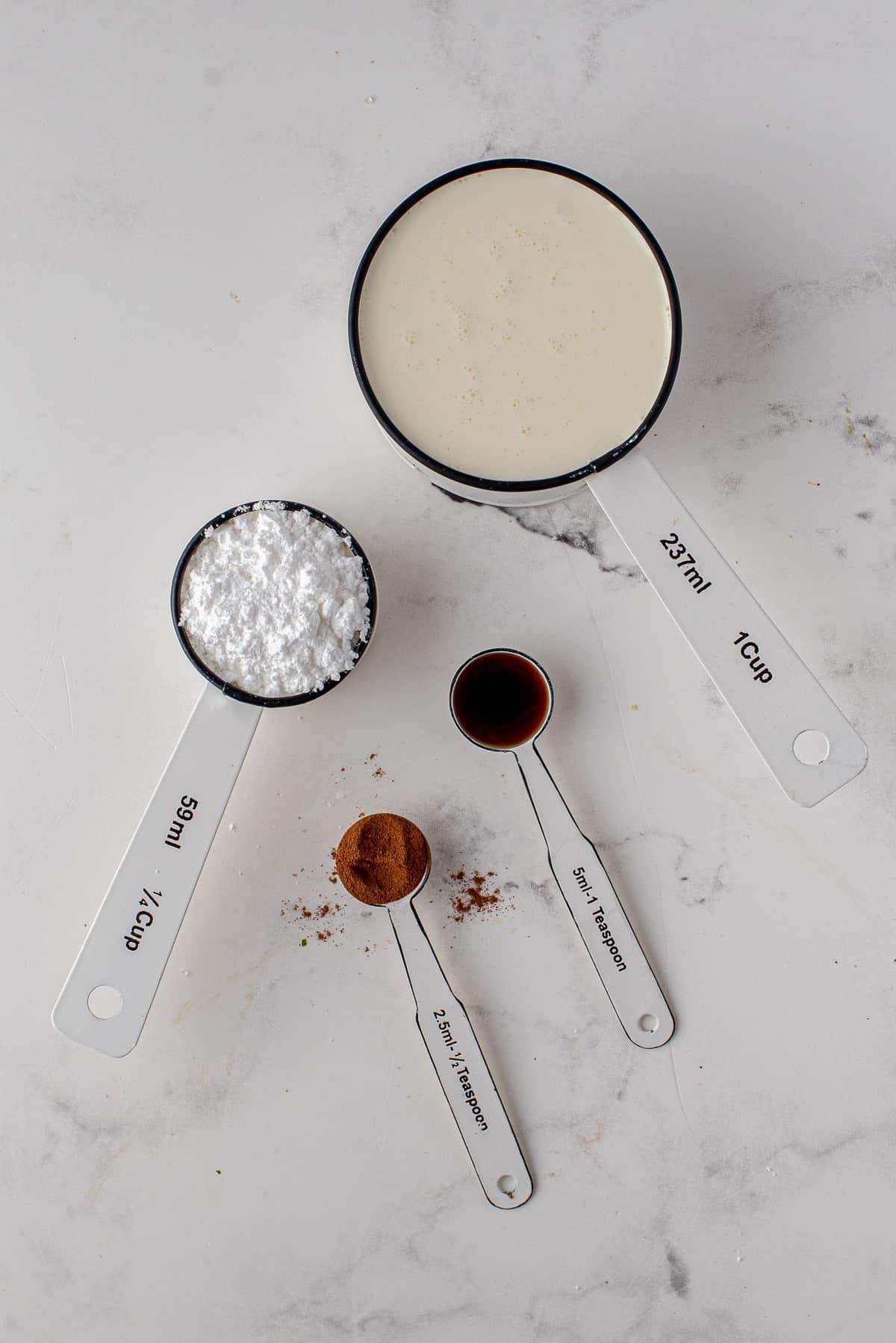 Crema, azúcar glas, canela y vainilla en utensilios de medición.