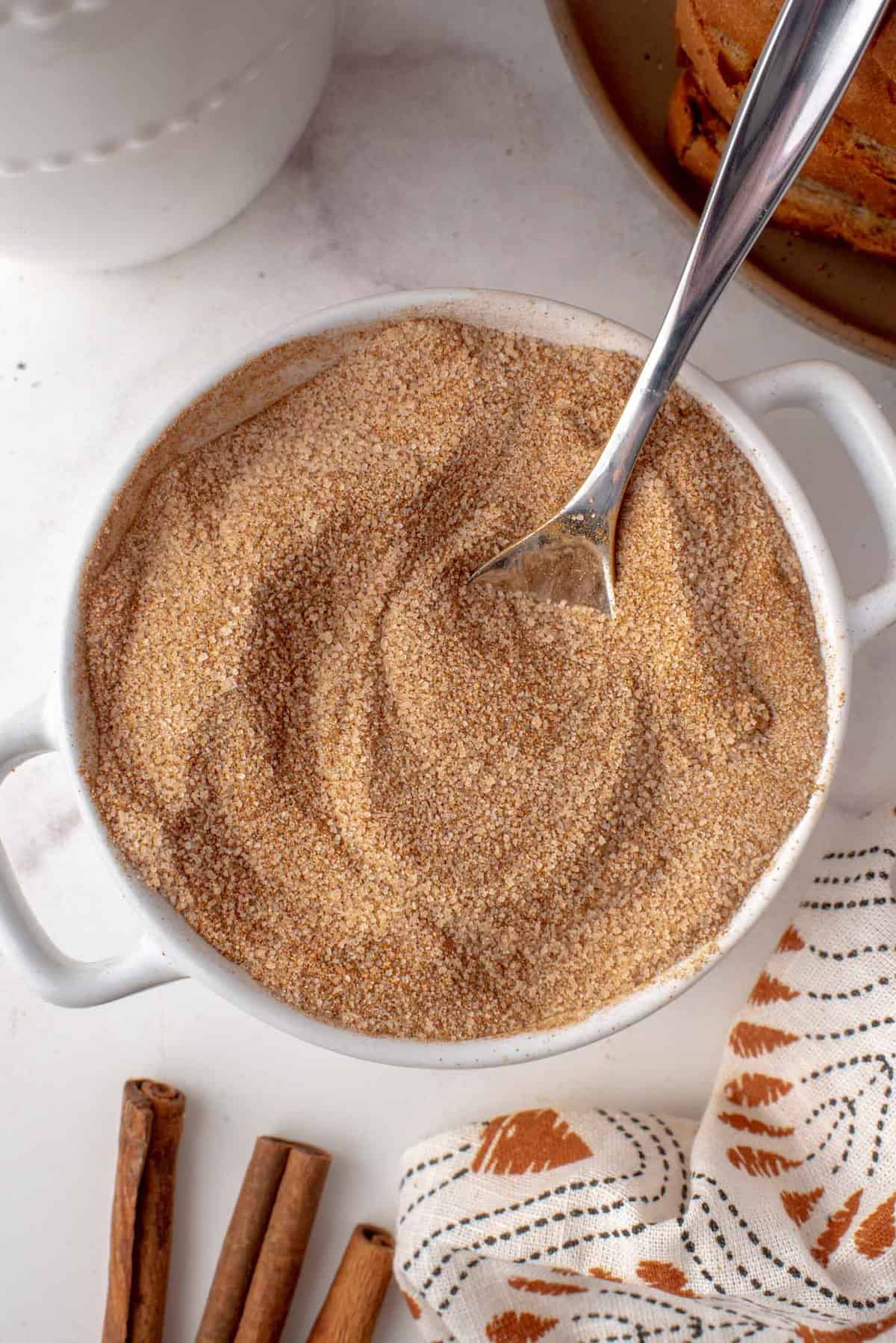 Azúcar de canela en un pequeño bol blanco con cuchara de plata.