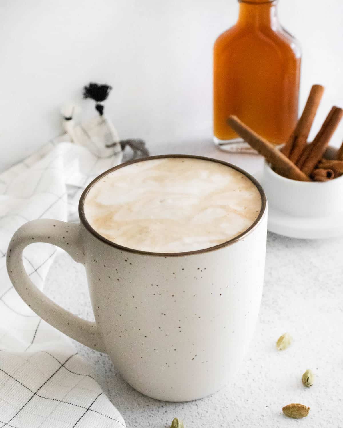 Café en una taza blanca con jarabe de café casero en el fondo.