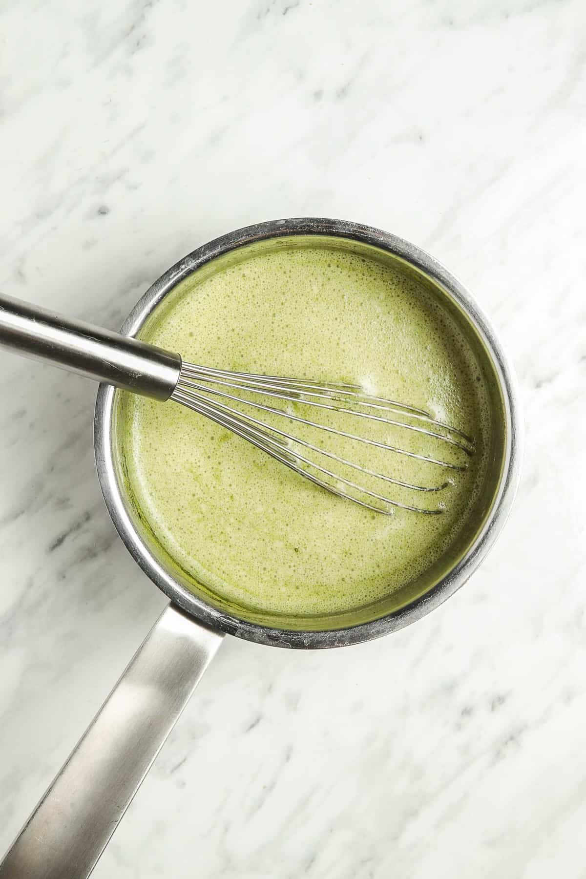 Chocolate caliente de matcha en una cacerola con un batidor.