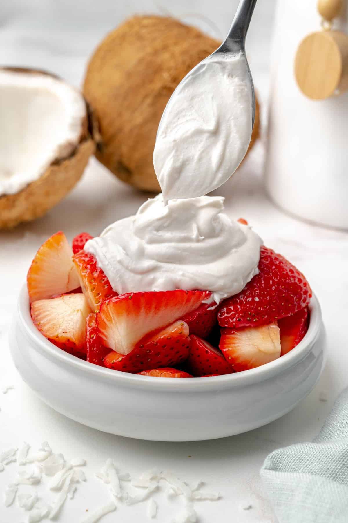 Crema batida de coco que se añade a un bol de fresas cortadas.