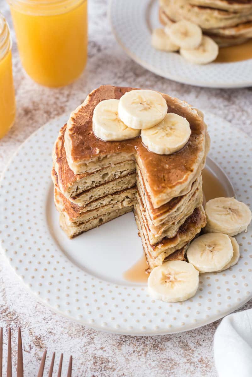 Montón de panqueques cubiertos con rodajas de plátano, con un trozo cortado.