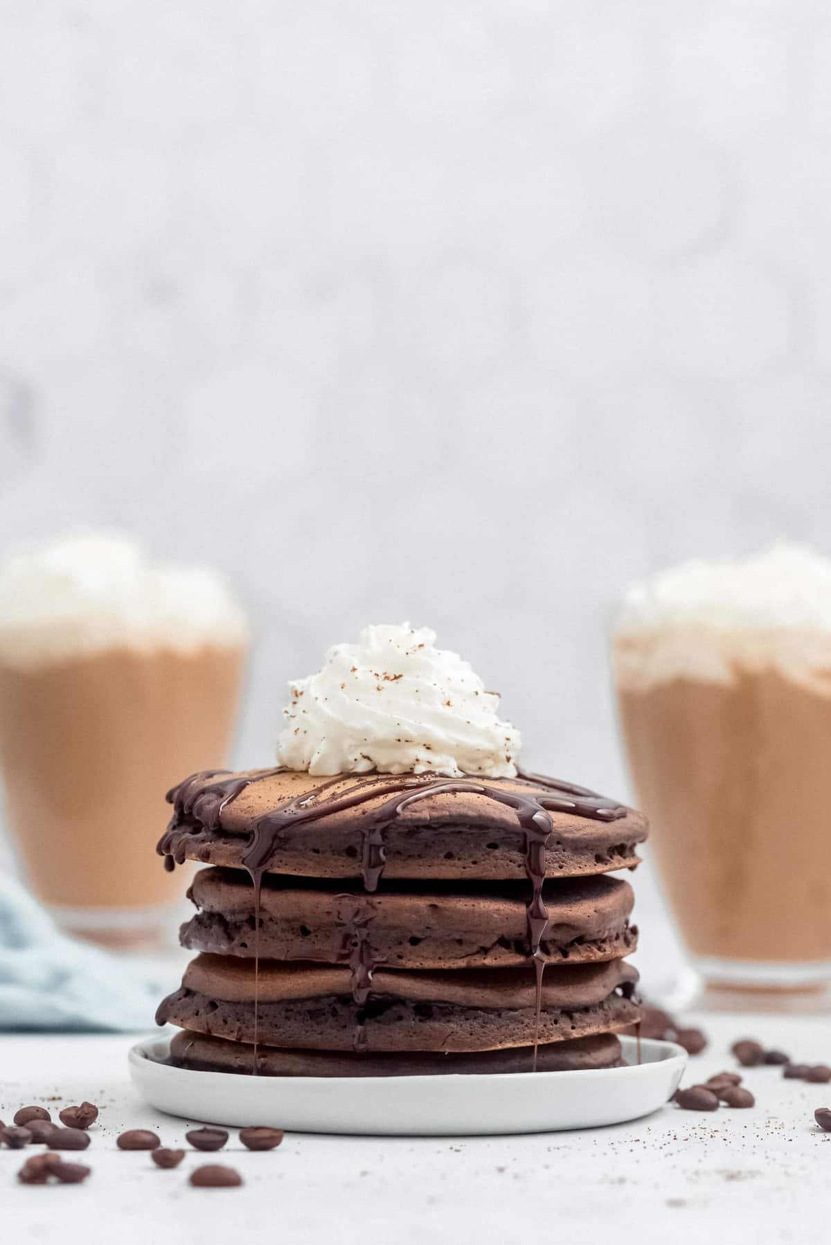 Pila de panqueques mocha con crema batida, con mochas de fondo.