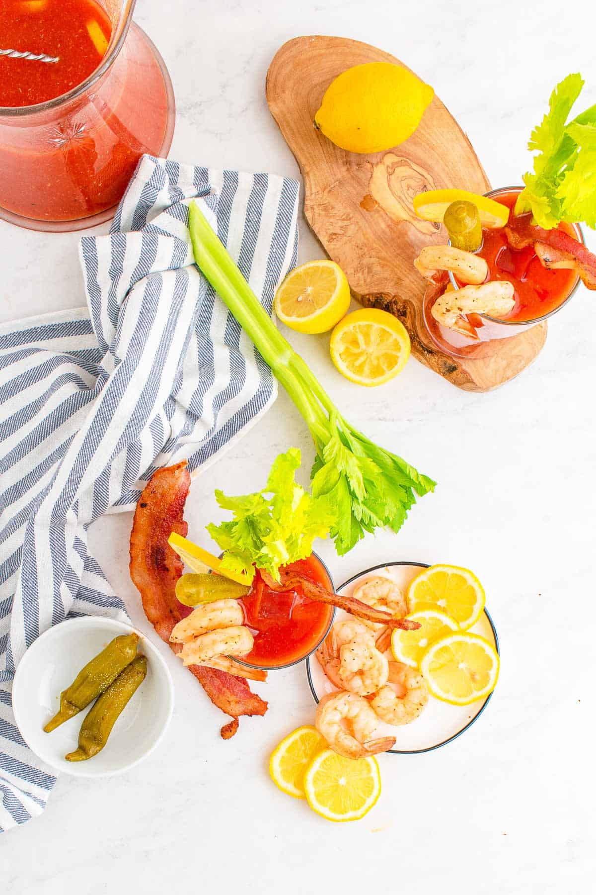 Vista cenital de bebidas a base de tomate con apio, ruedas de limón, camarones y bacon.