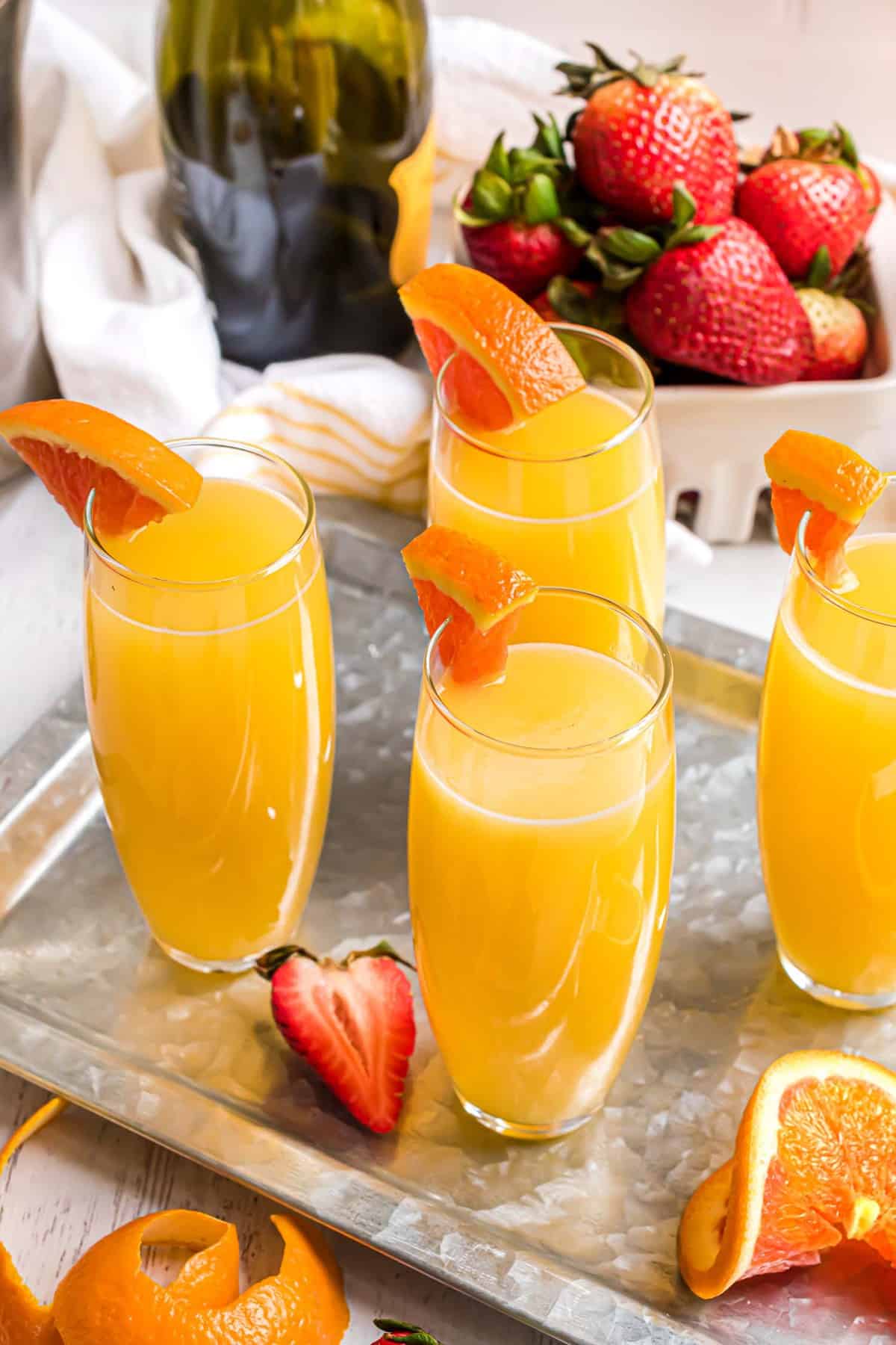 Bandeja de cócteles mimosa con jugo de naranja y una rodaja de naranja como adorno.