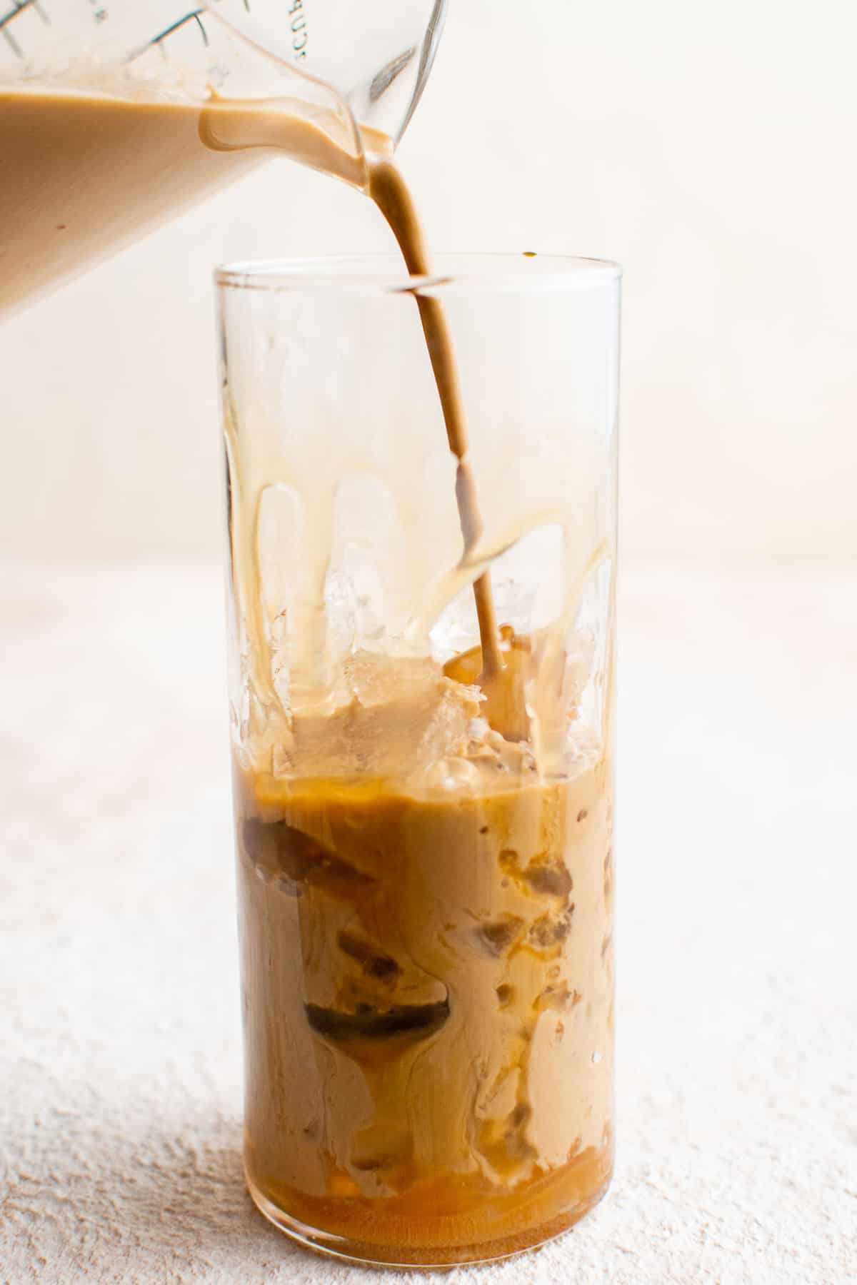Café latte vertiendo sobre hielo en un vaso alto y claro.