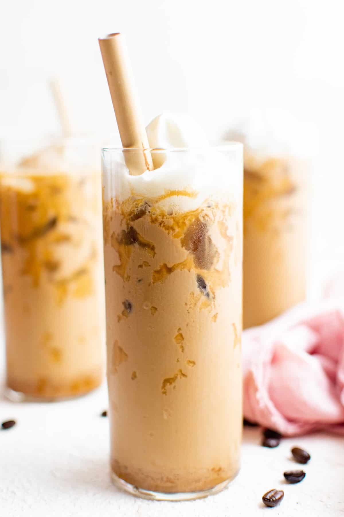 Latte helado, cubierto con crema batida, en un vaso alto con una pajita marrón.