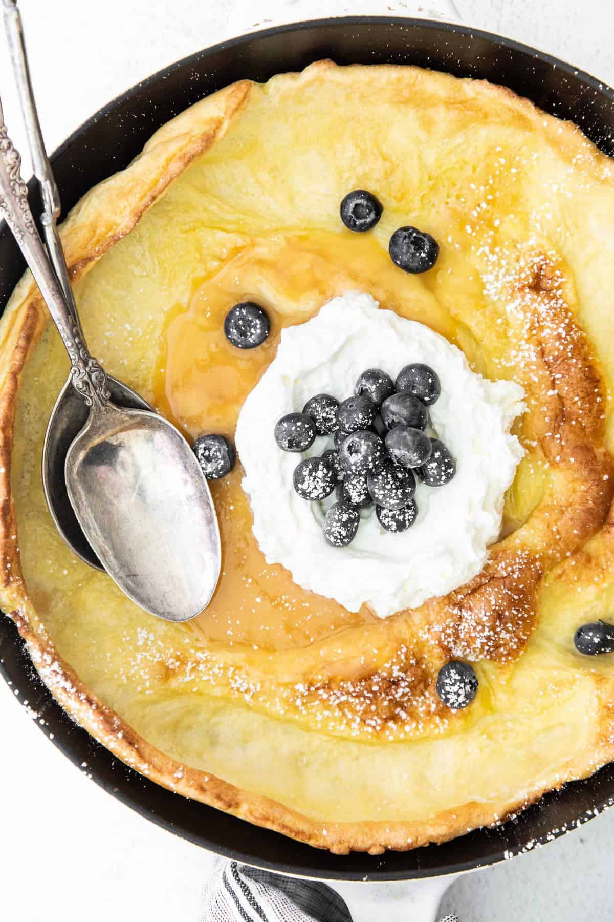 Primer plano de un panqueque holandés cubierto con crema de limón y arándanos.
