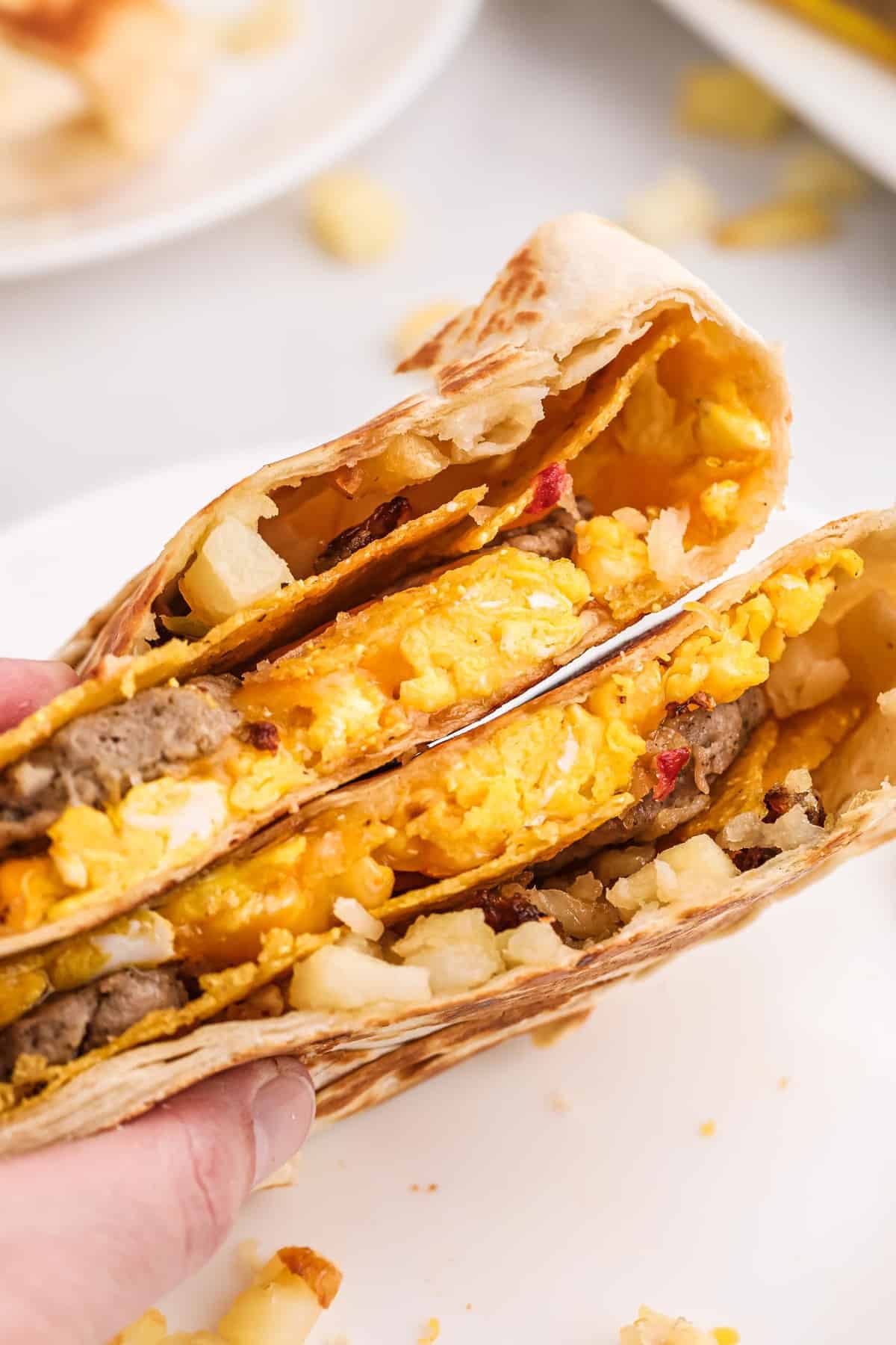 Mano sosteniendo dos mitades de un crunchwrap de estilo desayuno.