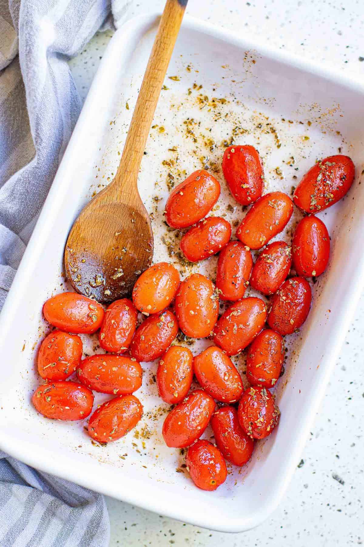 Tomates y condimentos en una bandeja de horno blanca.
