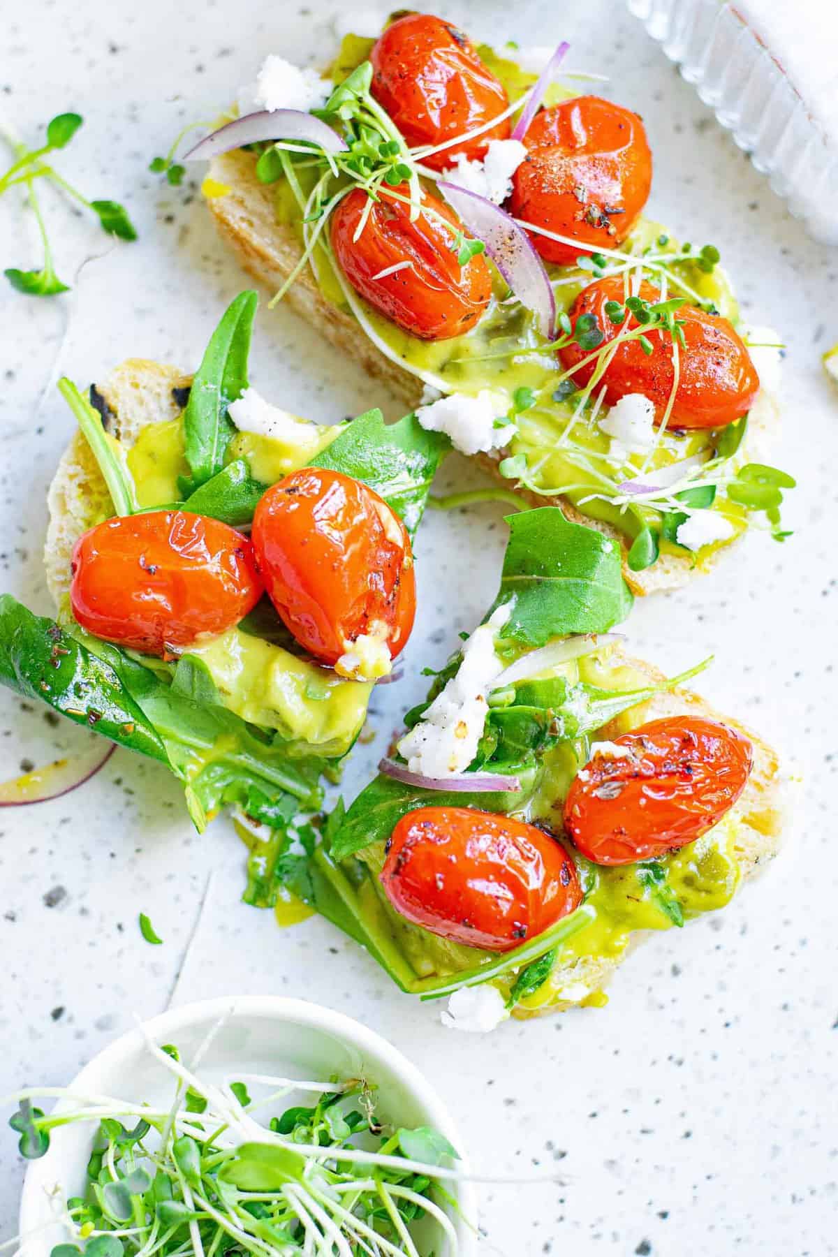 Tostada cubierta con guacamole, tomates, feta y hojas verdes.