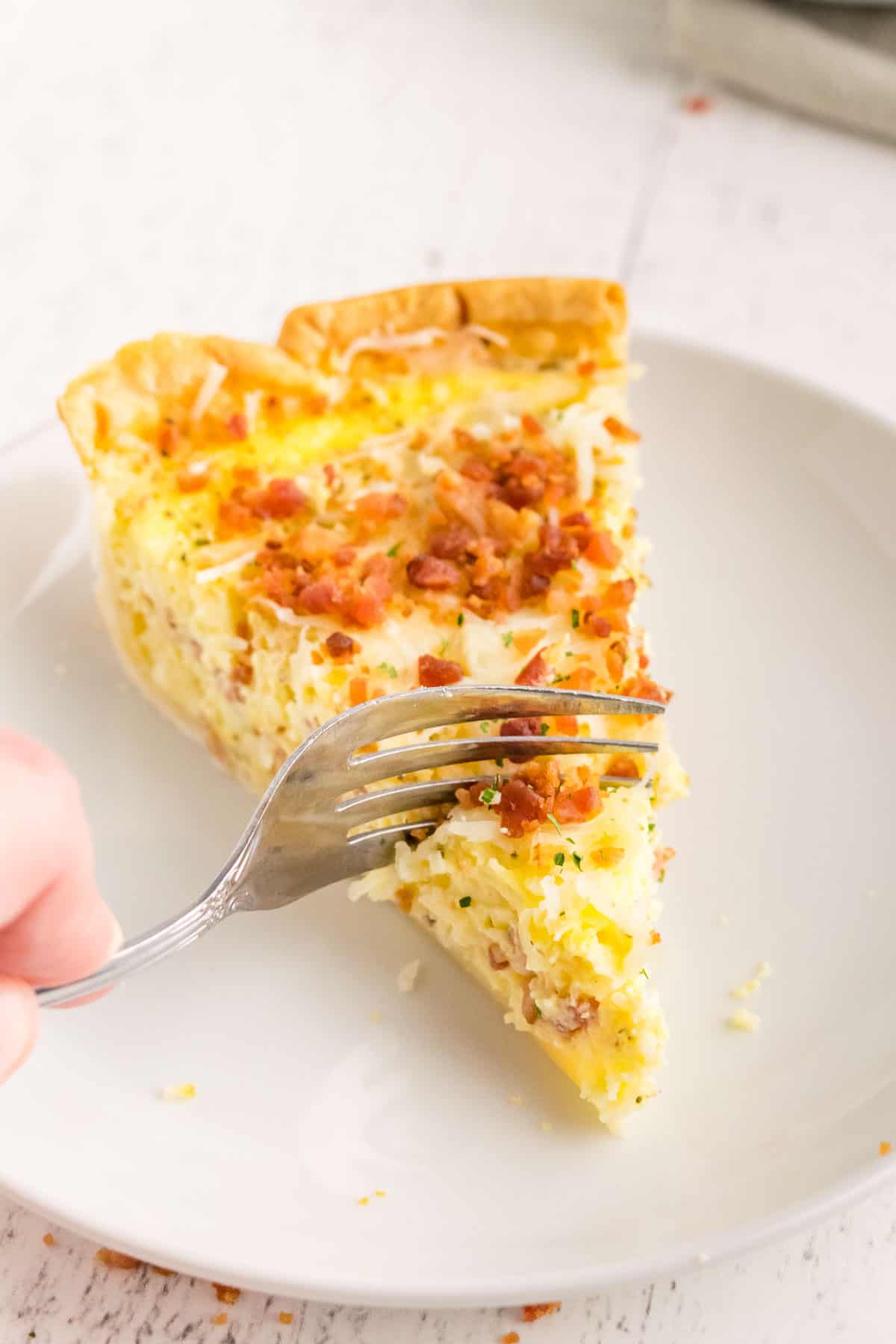 Porción de quiche en un plato blanco, un tenedor cortándolo.