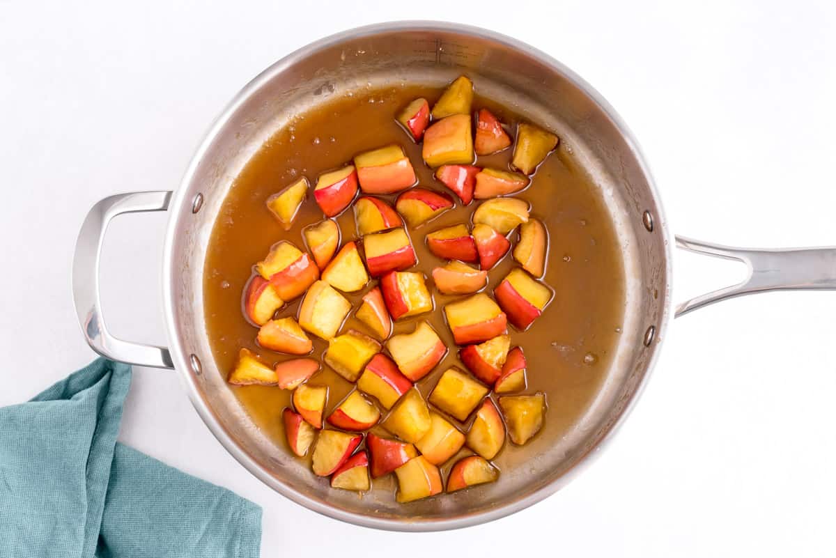Manzanas cocidas en una salsa de azúcar moreno en una sartén de acero inoxidable.