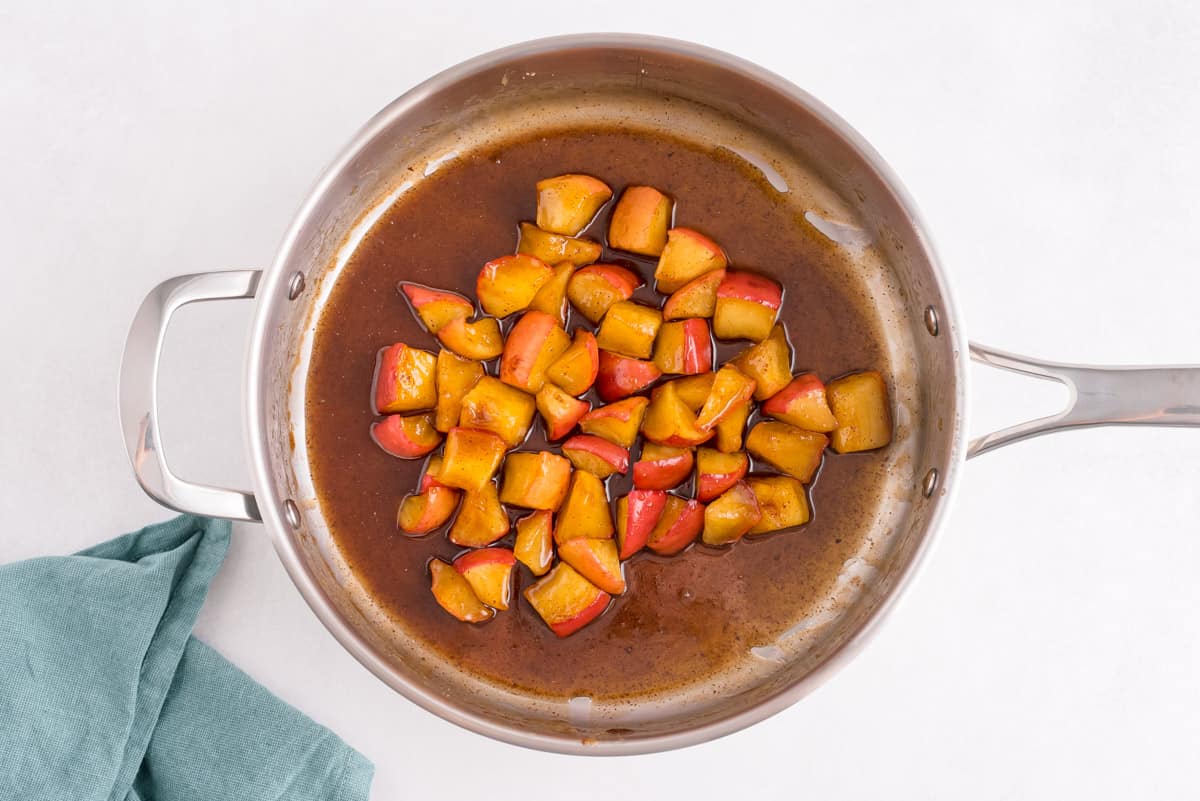 Trozos de manzana con canela en una salsa de azúcar moreno, en una sartén.