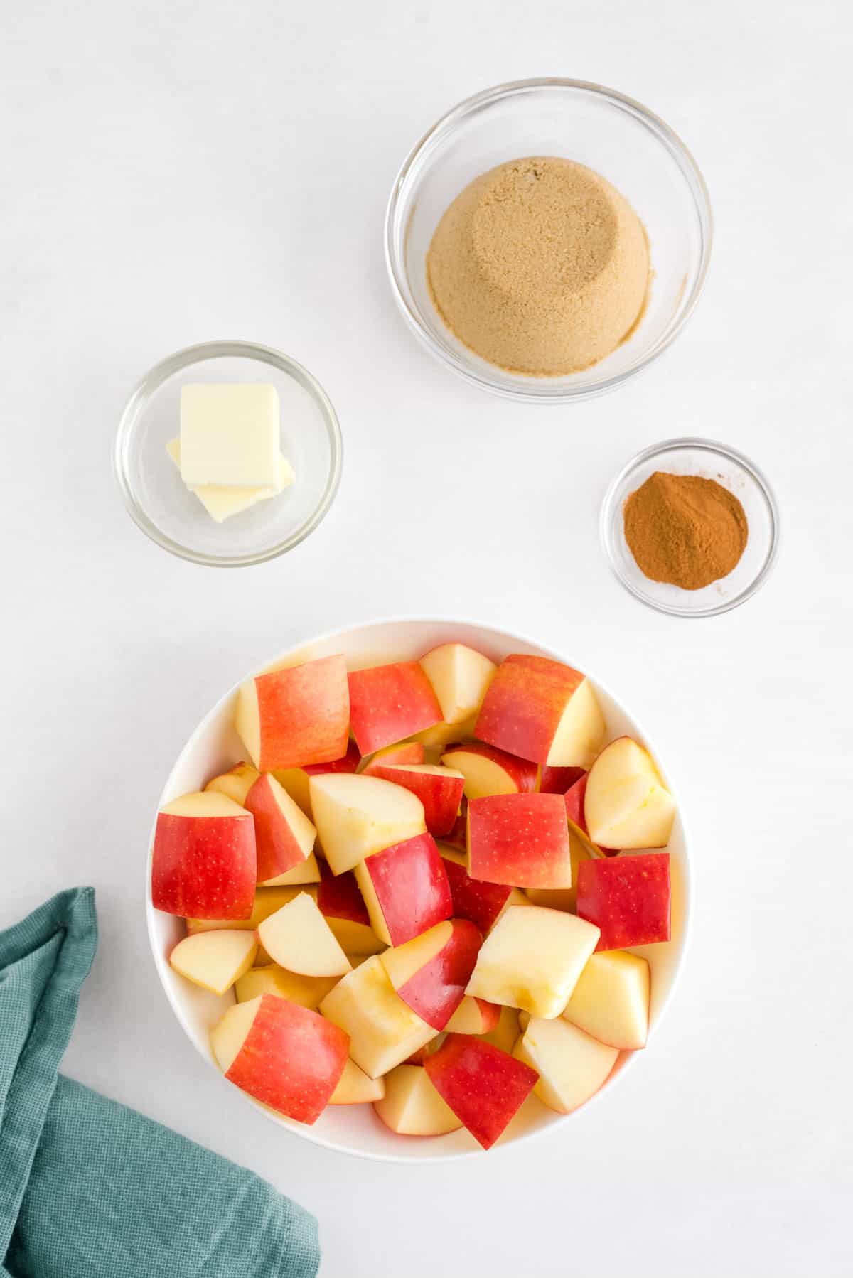 Cuatro cuencos llenos de ingredientes: manzanas picadas, mantequilla, azúcar moreno y canela.