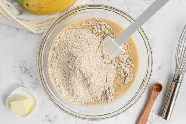 Ingredientes secos encima de los ingredientes húmedos en un tazón de vidrio.