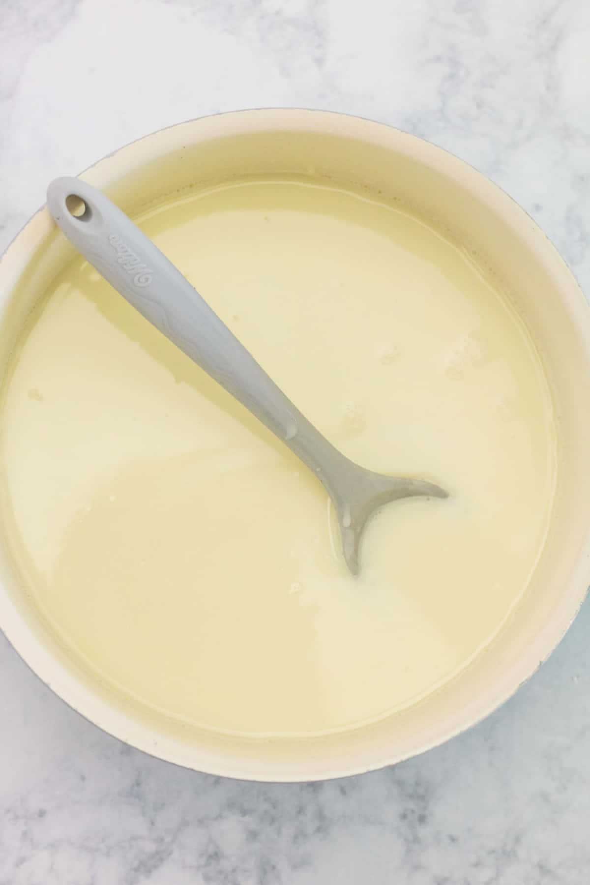 Chocolate blanco caliente en una sartén con una cuchara.