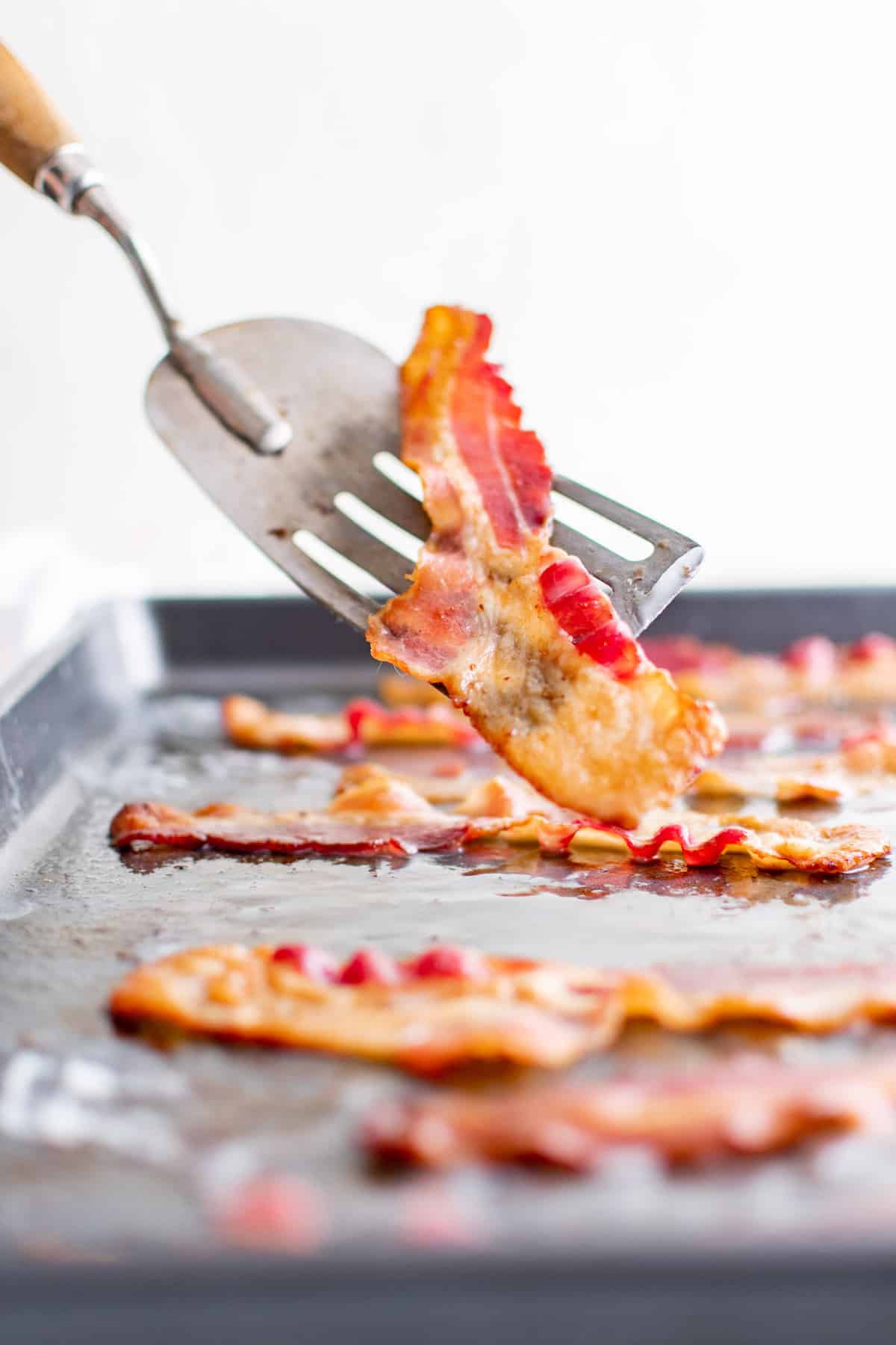 Panceta crujiente en una espátula, más en una bandeja para hornear en el fondo.