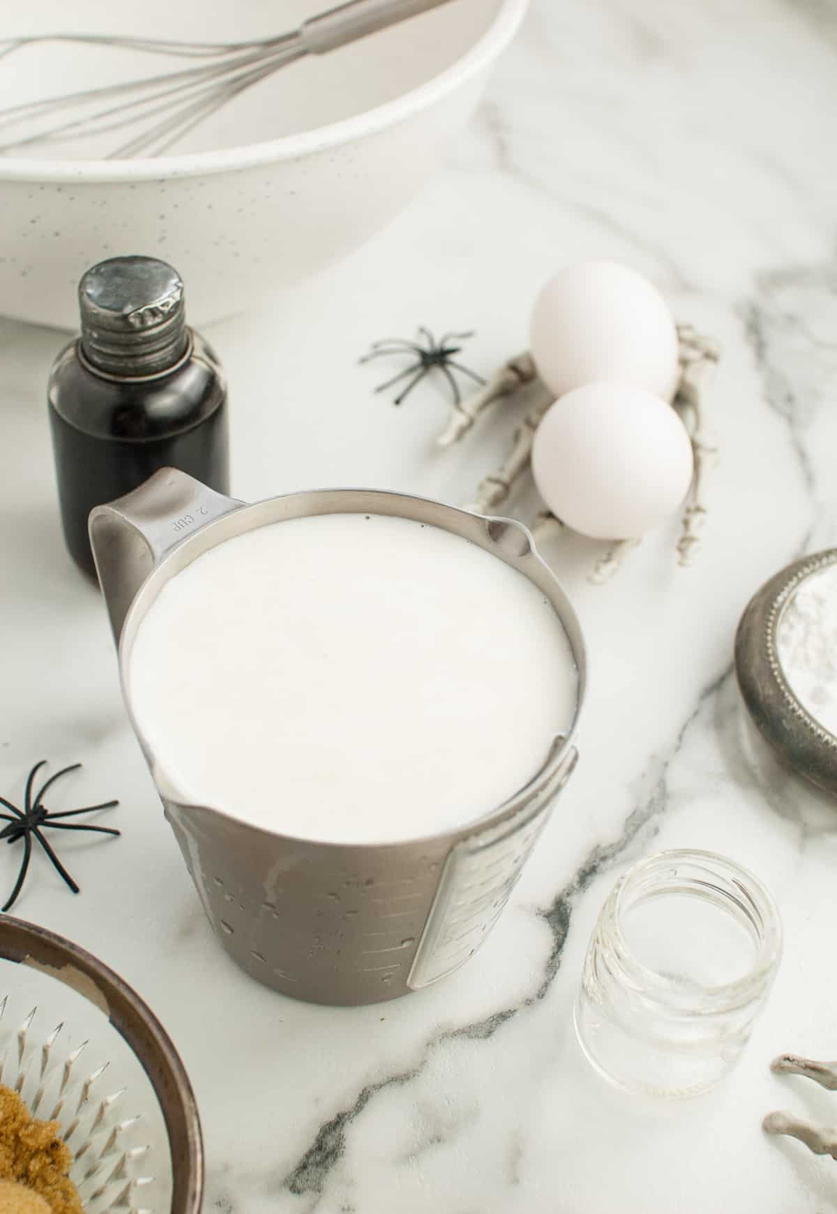 Leche en una taza medidora de metal, otros ingredientes cerca.