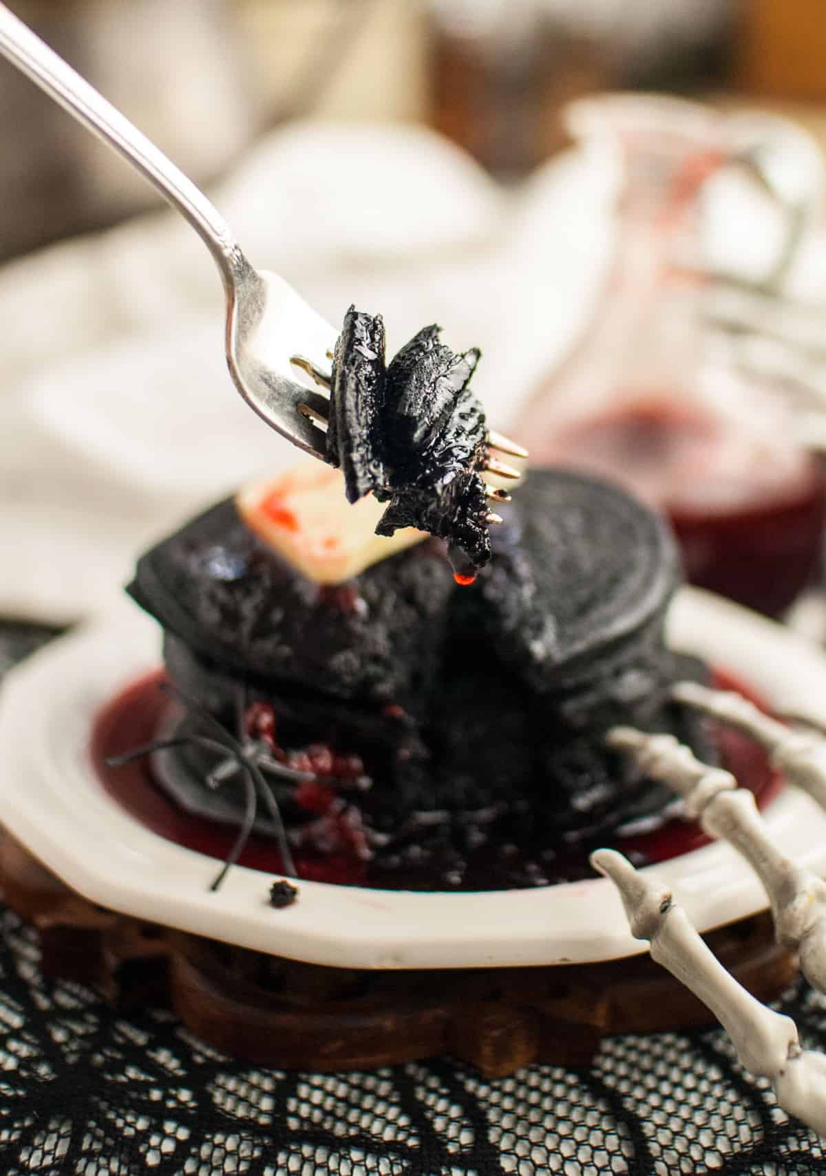 Panqueques negros en un tenedor, con una mano de esqueleto en primer plano.