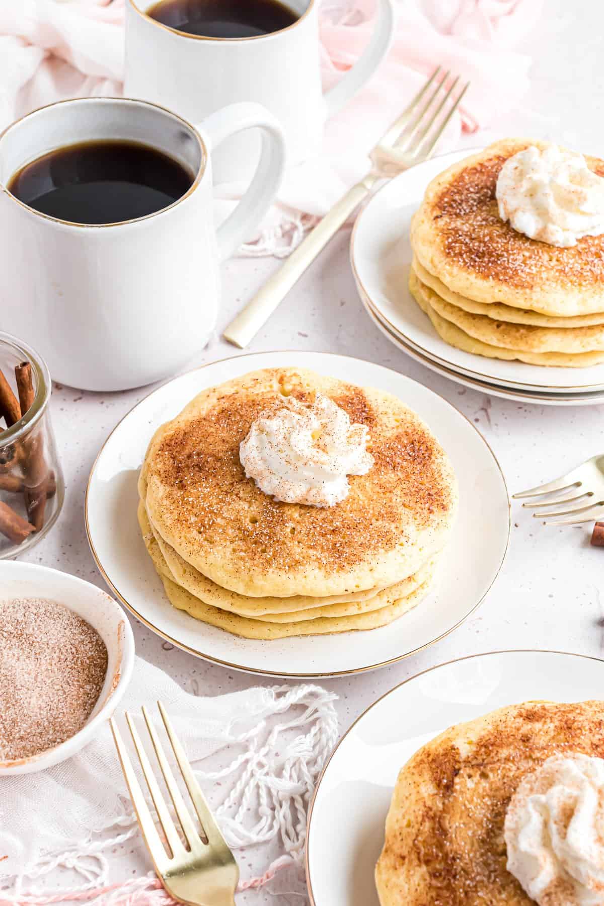 Panqueques, café, tenedores y crema batida en una mesa.