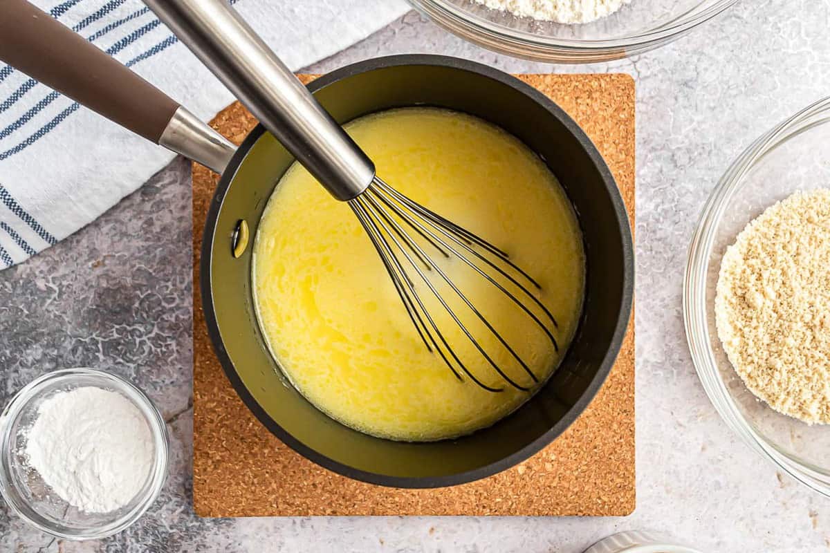 Ingredientes húmedos en una cacerola con un batidor de alambre.
