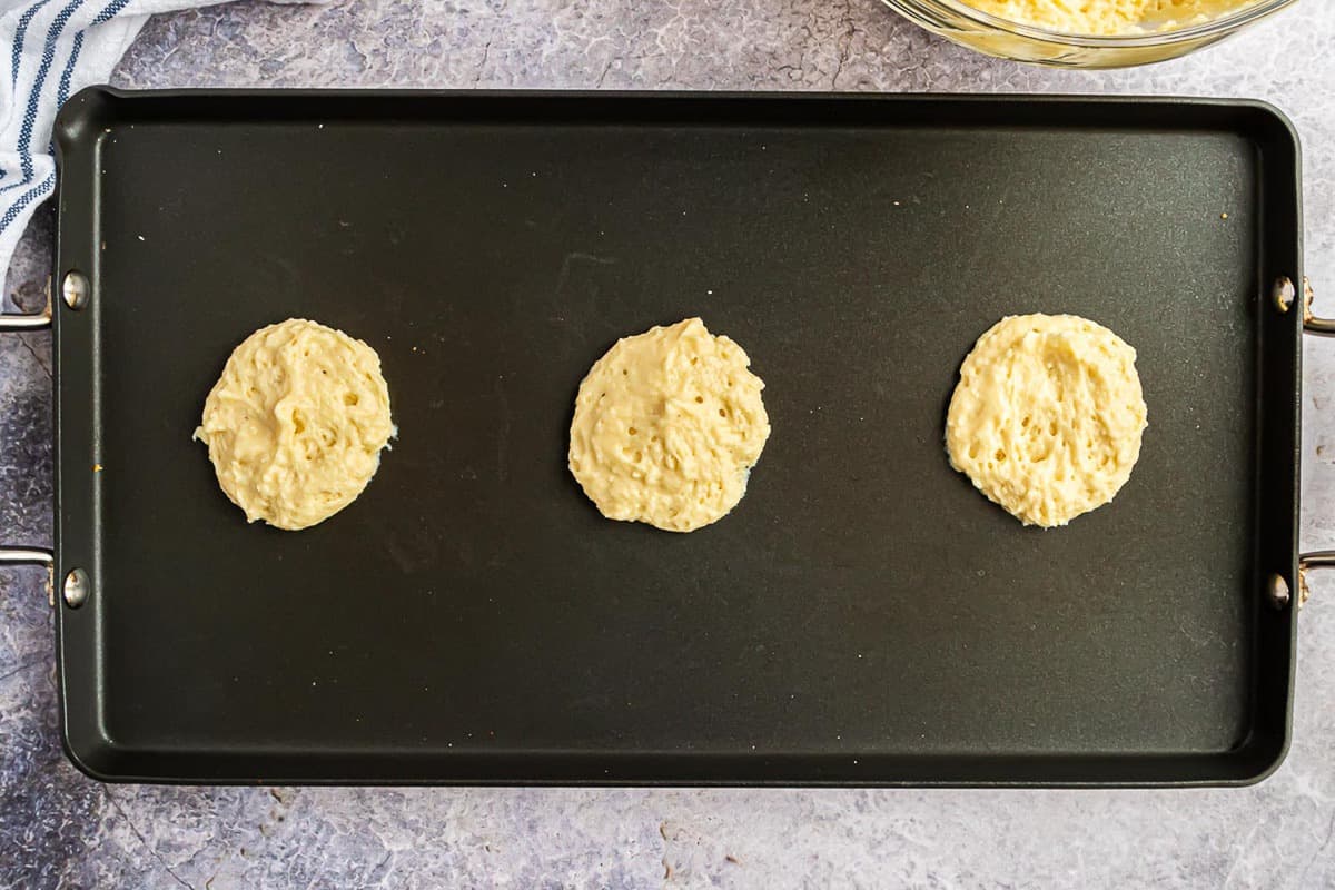 Tres panqueques, medio cocidos, en una plancha.