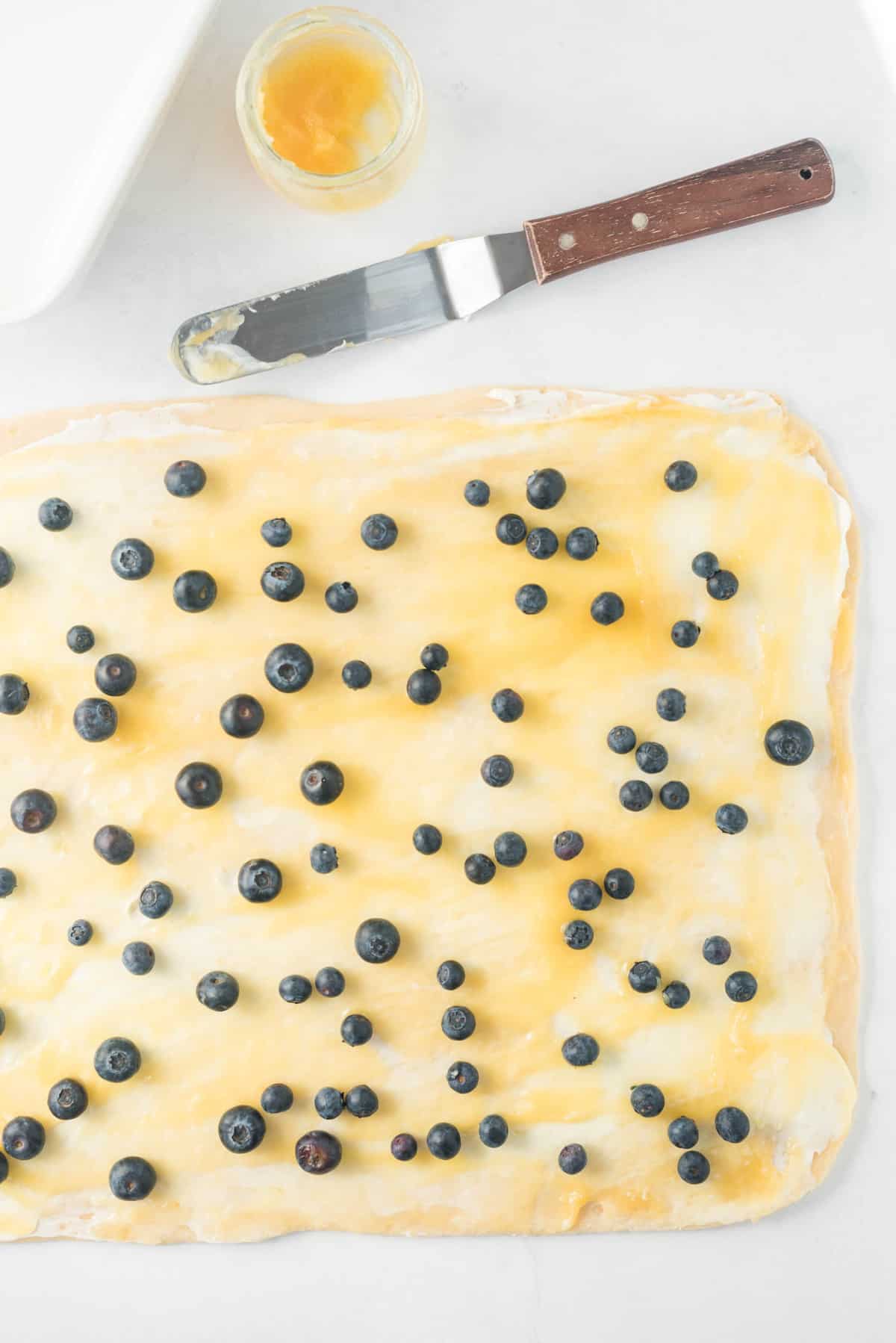 Masa cubierta con queso crema, crema de limón y arándanos.