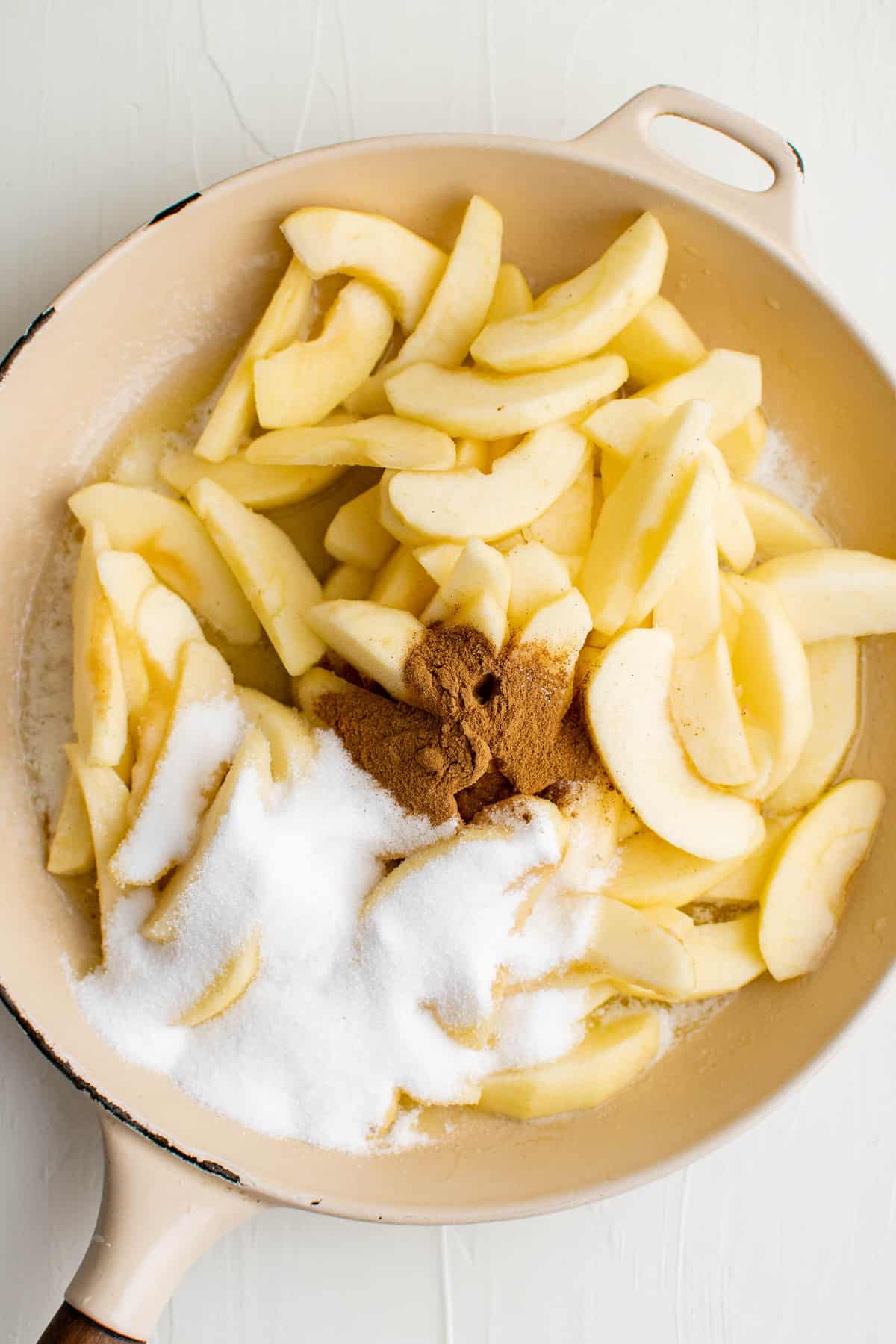 Manzanas, azúcar, especias y mantequilla en una sartén blanca.